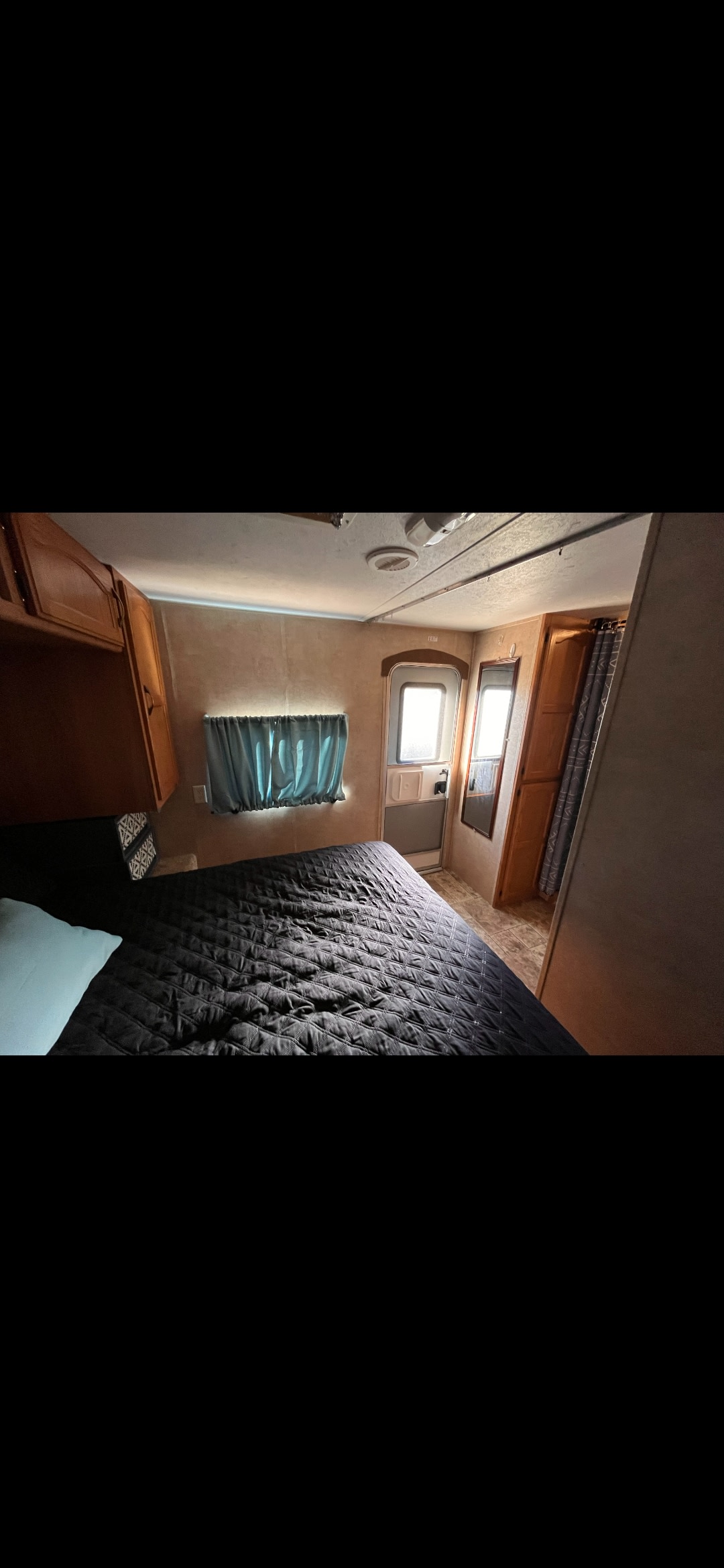 This cozy RV rental features a comfortable bedroom with a black quilted bed, blue window curtains, and built-in cabinets.. Keystone RV Summerland 2011