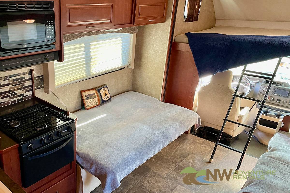 RV rental interior: Kitchen with stove, microwave, and two sleeping areas (lower bed, overhead bunk with ladder).. Winnebago Minnie Winnie 2015