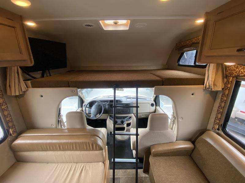 RV rental interior showing an overhead bunk, driver's cab, and spacious living area with seating and TV.. Thor Freedom Elite 2016