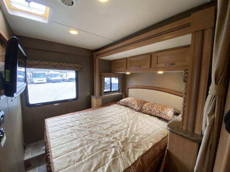 Cozy RV rental bedroom: features a comfortable bed, mounted TV, overhead cabinets, and windows, showcasing comfort.. Thor Freedom Elite 2016