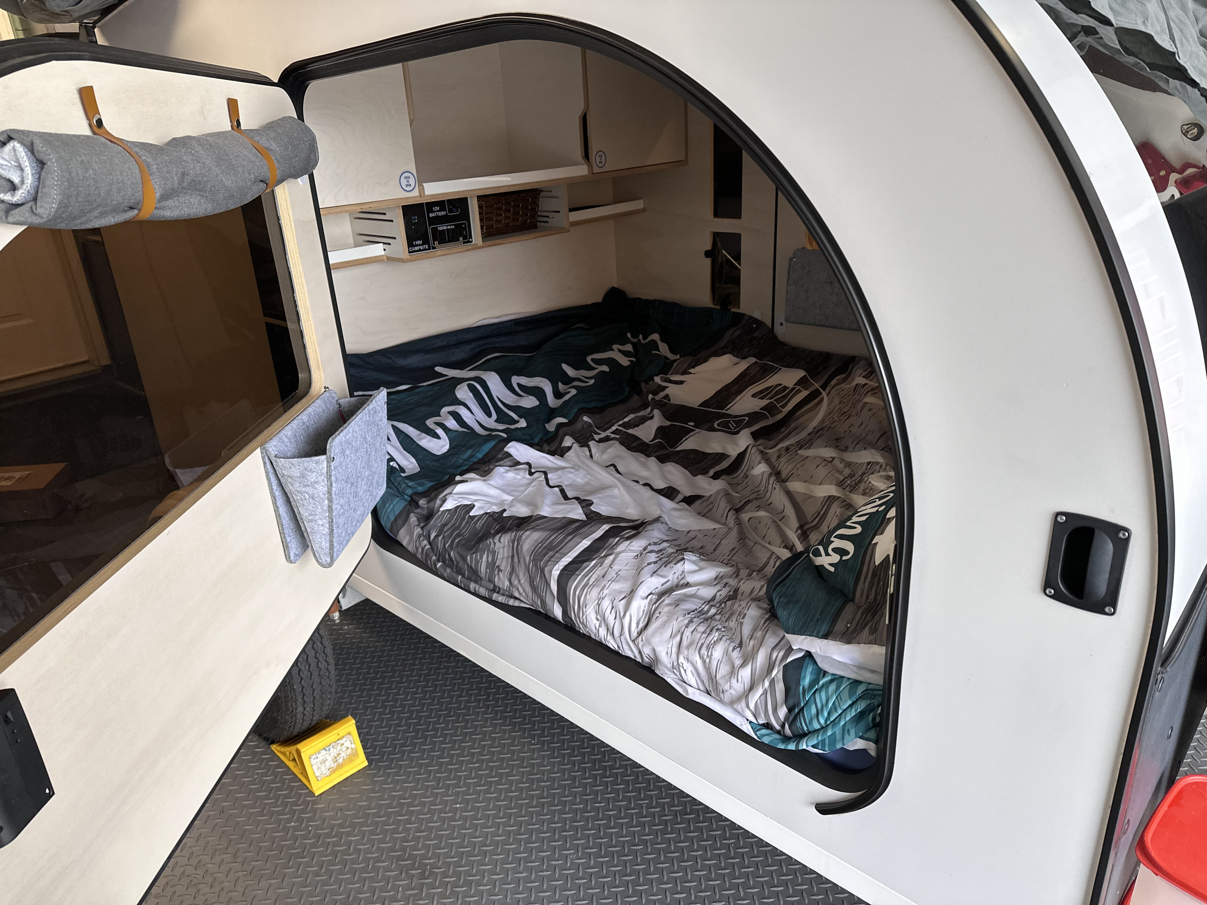 Cozy RV rental interior: A compact teardrop camper's sleeping area with bed, built-in storage, and power access.. Droplet 58 2021