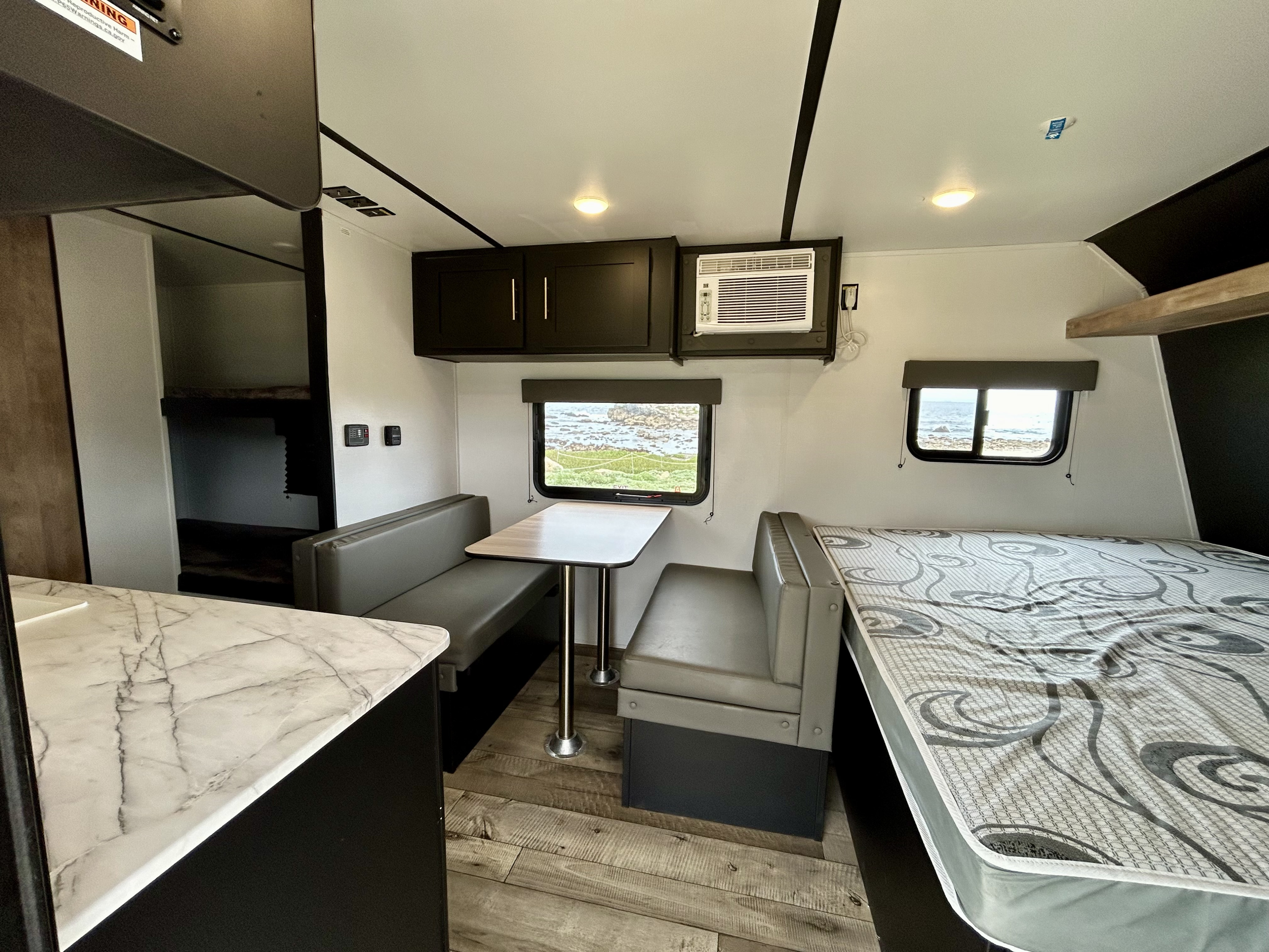 Compact rv rental interior featuring a dinette, bed, and bunk beds with a small kitchen area and ocean view.. Keystone Springdale 2022