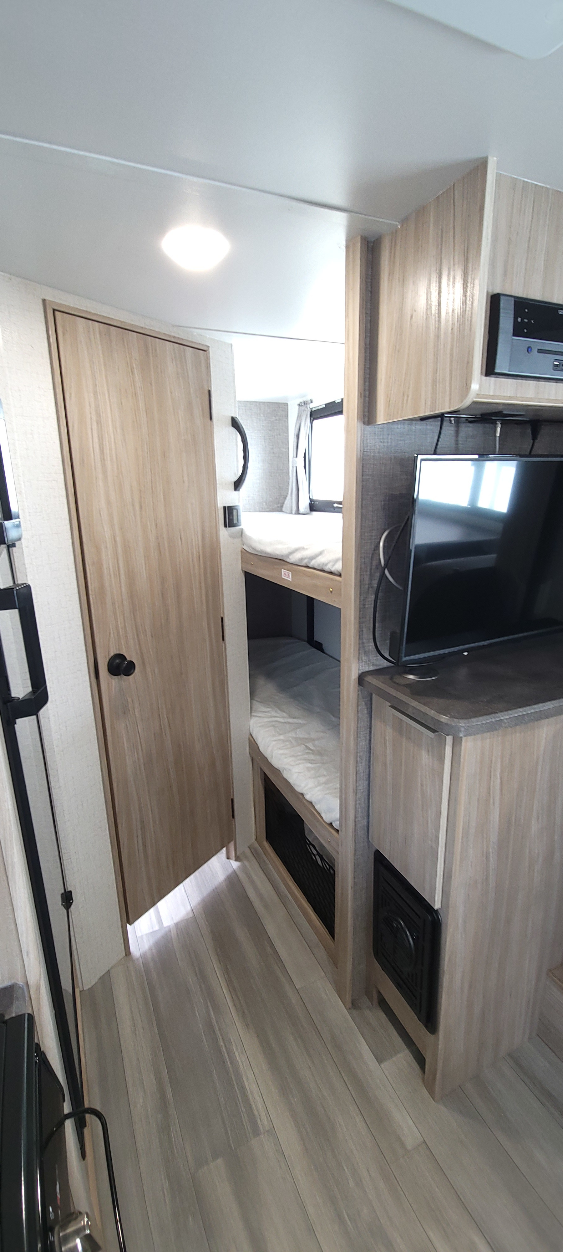 Inside an RV rental: a bunk bed with white bedding, TV, stereo, and light wood door leading to another area.. Winnebago Micro Minnie 2021
