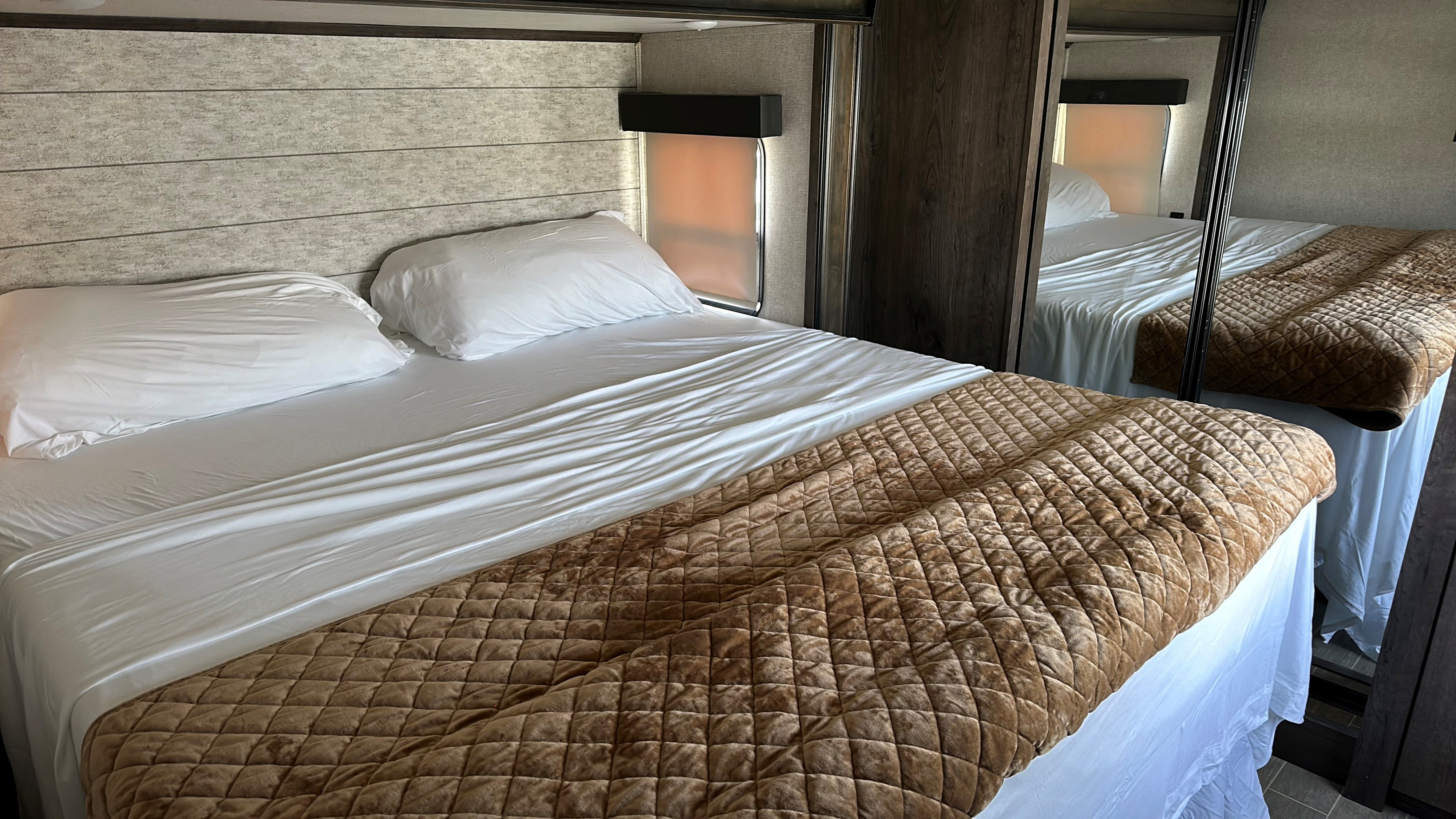 Cozy RV rental bedroom with a comfortable bed, white linens, and quilted brown blanket.. Keystone RV Montana High Country 2019