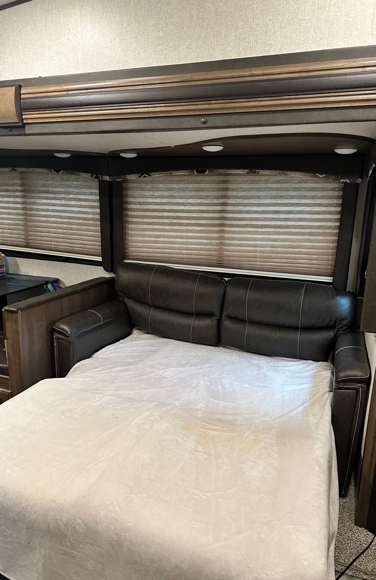 A dark leather sofa pulled out as a bed in an RV rental, covered by a light blanket, with blinds visible.. Keystone RV Cougar 2018