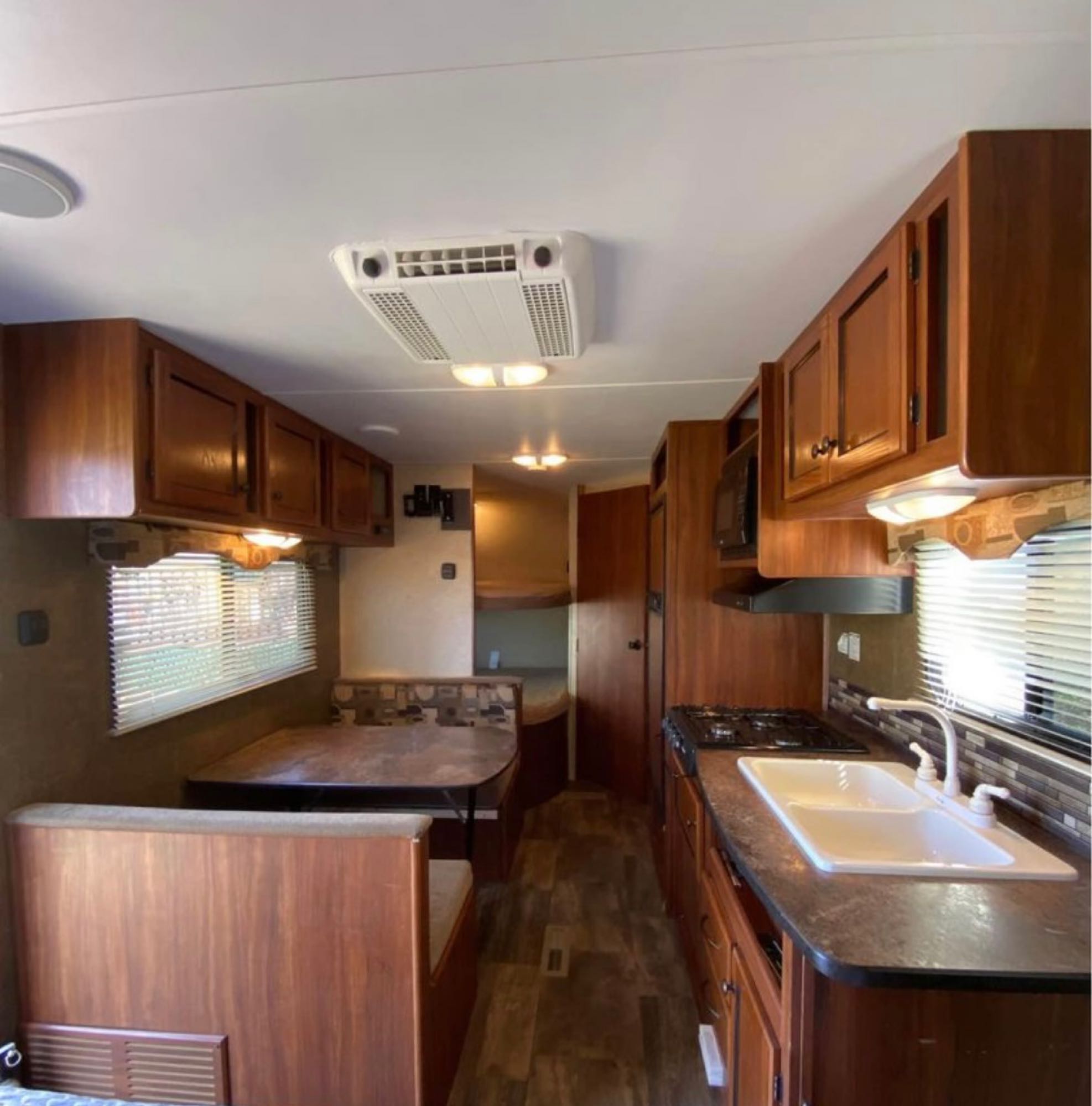 RV rental interior: wood cabinets, kitchen with sink & stovetop, dinette. Features AC, microwave, and bunk beds visible.. Heartland RVs Trail Runner 2014