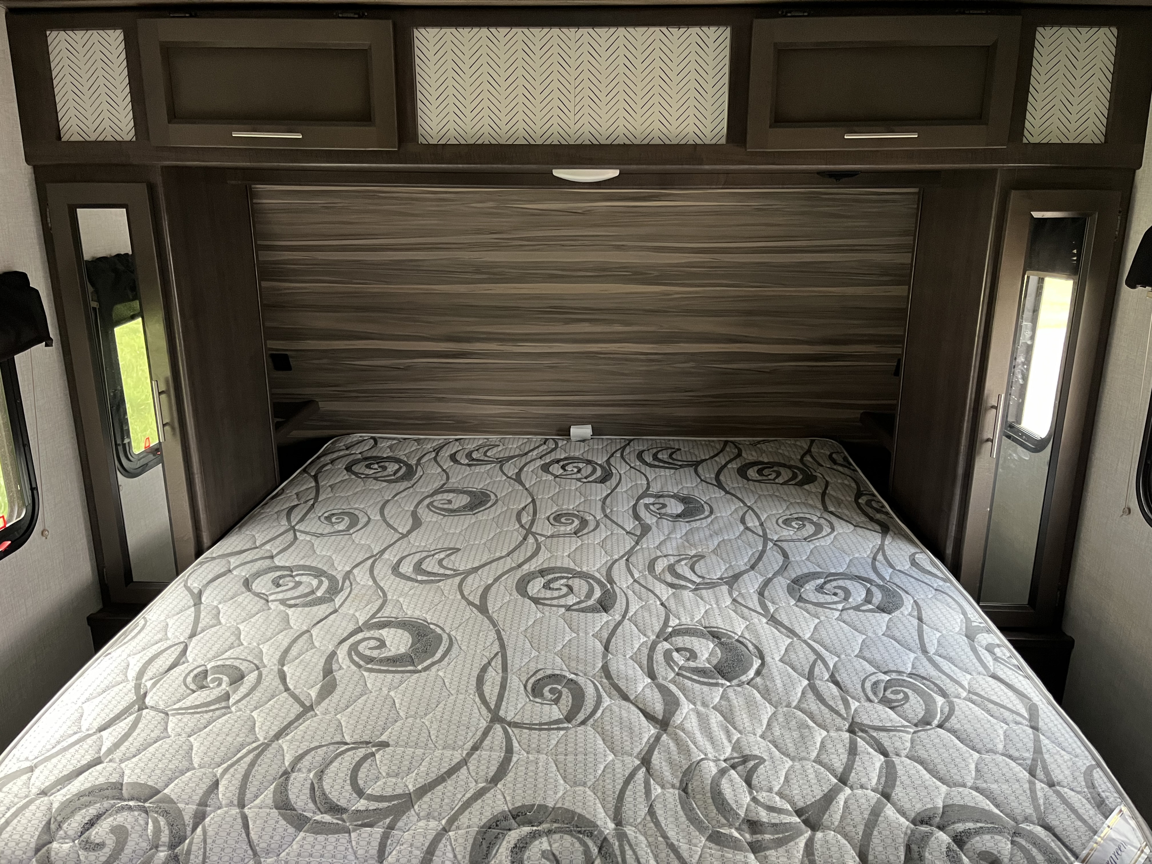 RV rental bedroom with patterned mattress, wood-look headboard, and chevron-accented overhead cabinets for storage.. Crossroads Sunset Trail 2020