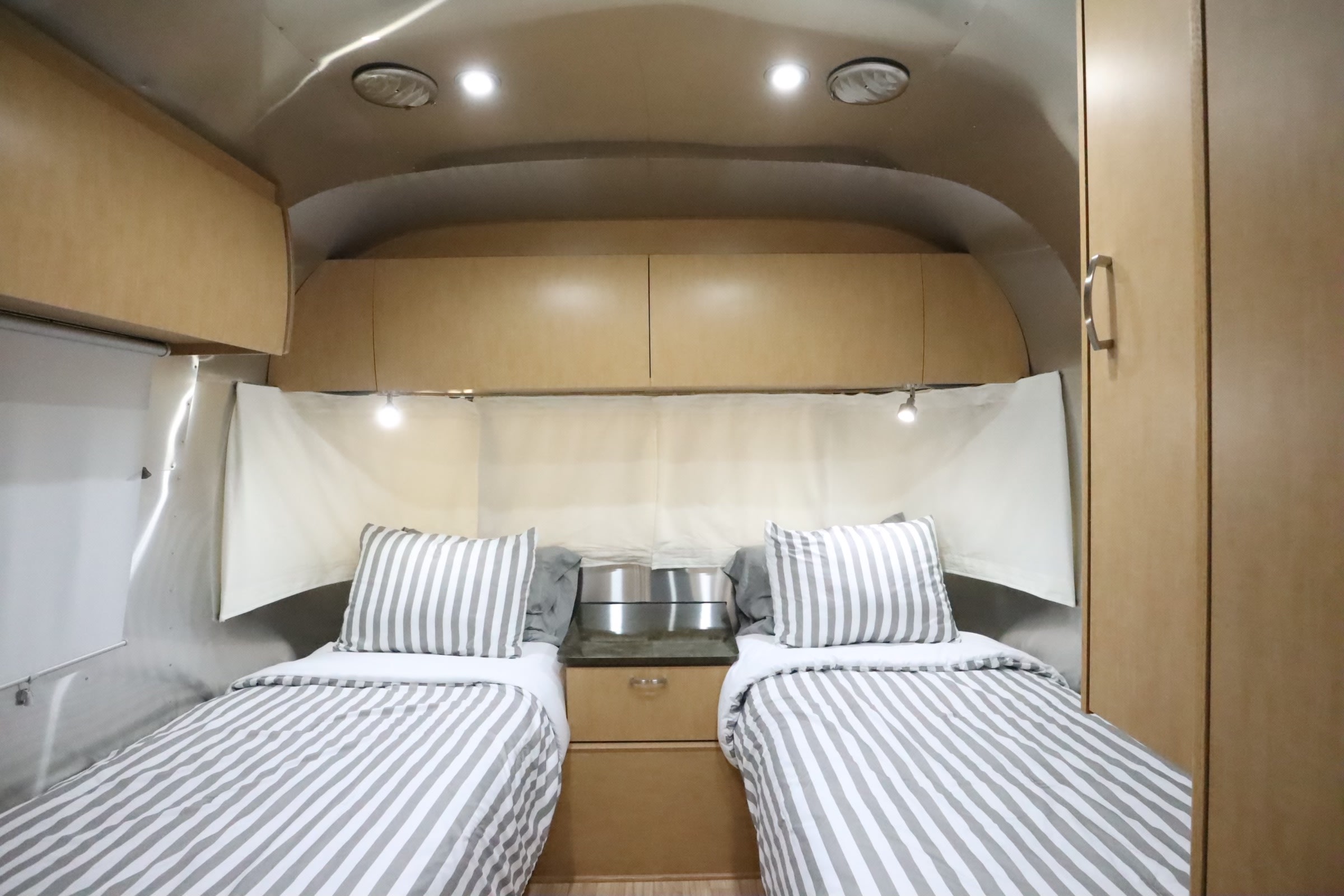 Spacious RV rental bedroom with two cozy twin beds, striped duvets, and ample overhead storage. Bright and functional.. Airstream Flying Cloud 2016
