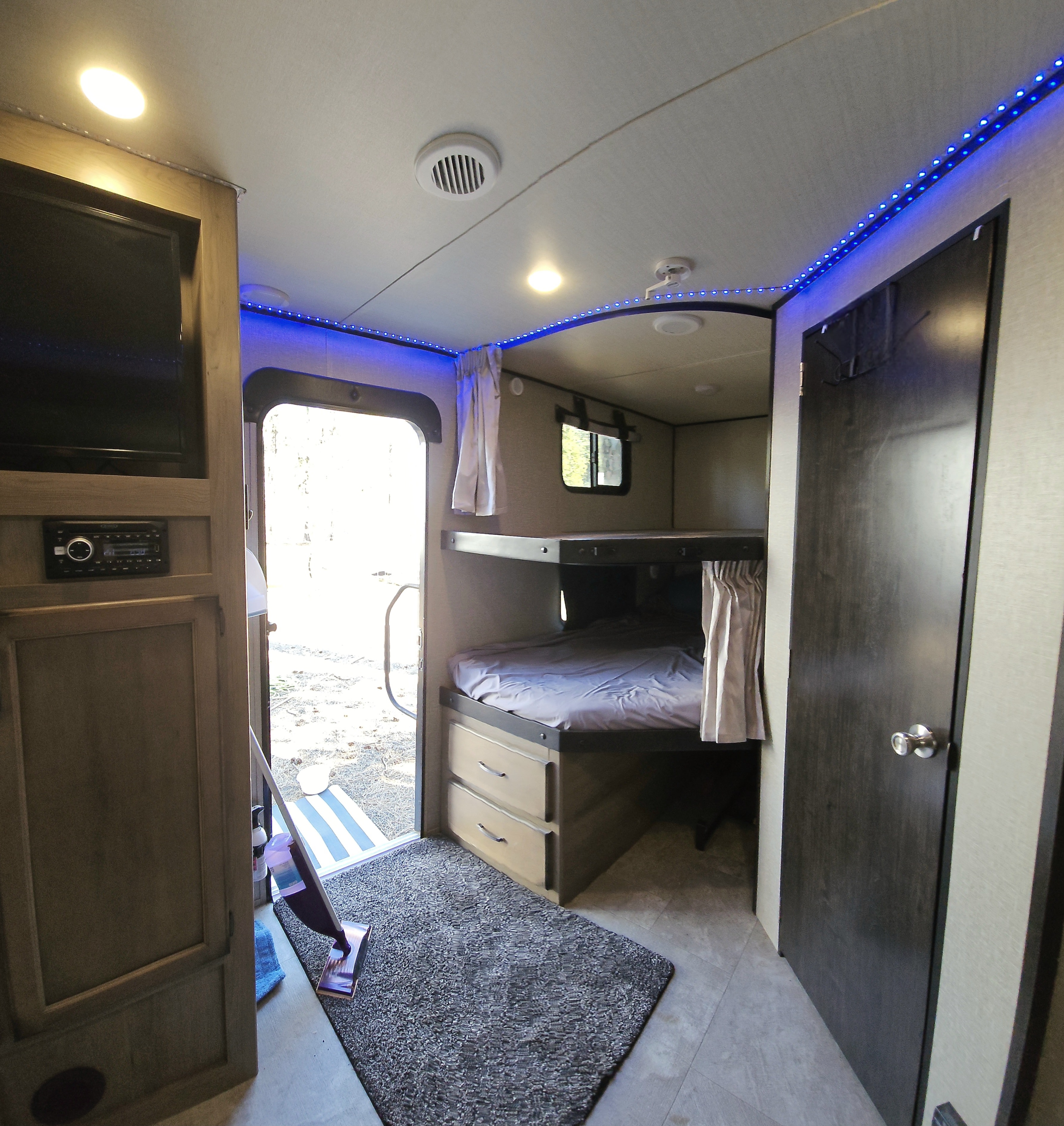 Inside an RV rental: view of bunk beds, blue LED lights, and entertainment system near the open entry door.. Grand Design Transcend 2019