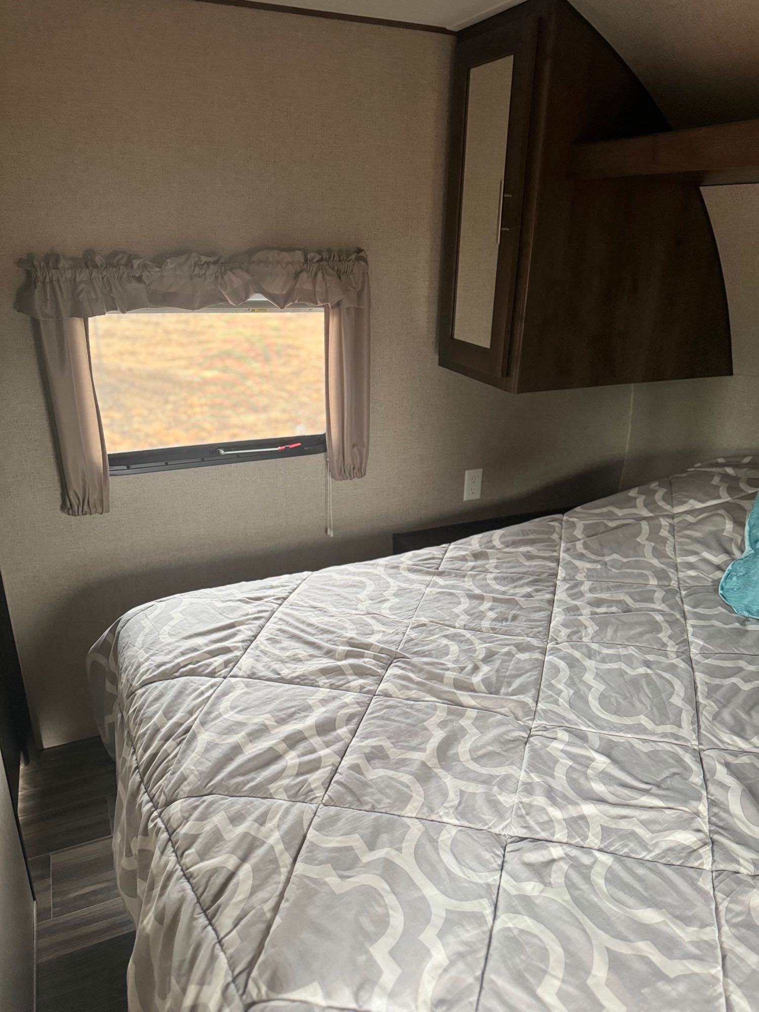 Cozy RV rental bedroom with a patterned comforter, window, and overhead storage, perfect for a comfortable travel stay.. Shasta 26db 2020