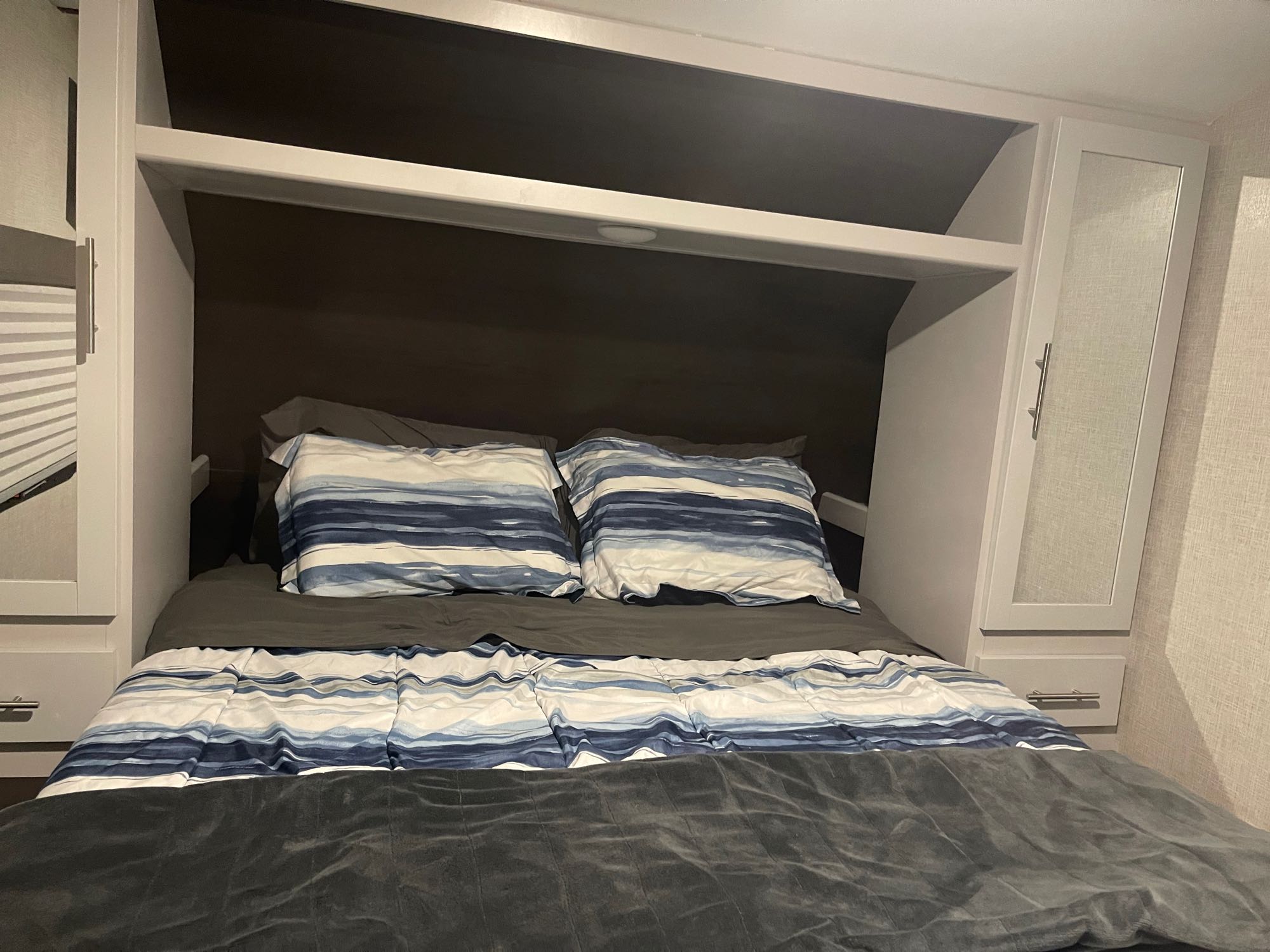 Cozy RV rental bedroom featuring a bed with blue and white striped bedding, overhead storage, and light cabinets.. Keystone RV Bullet Ultra Lite 2021