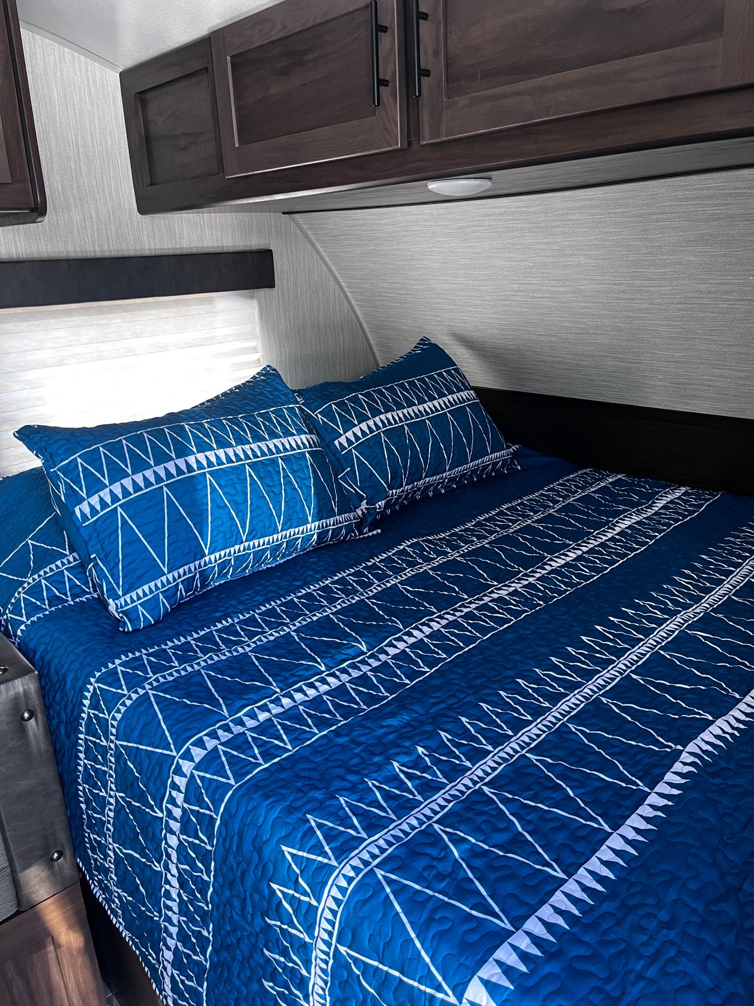 Comfortable RV rental bedroom with blue geometric bedding & dark wood cabinets. Ready for travel!. Forest River Cherokee Wolf Pup 2020