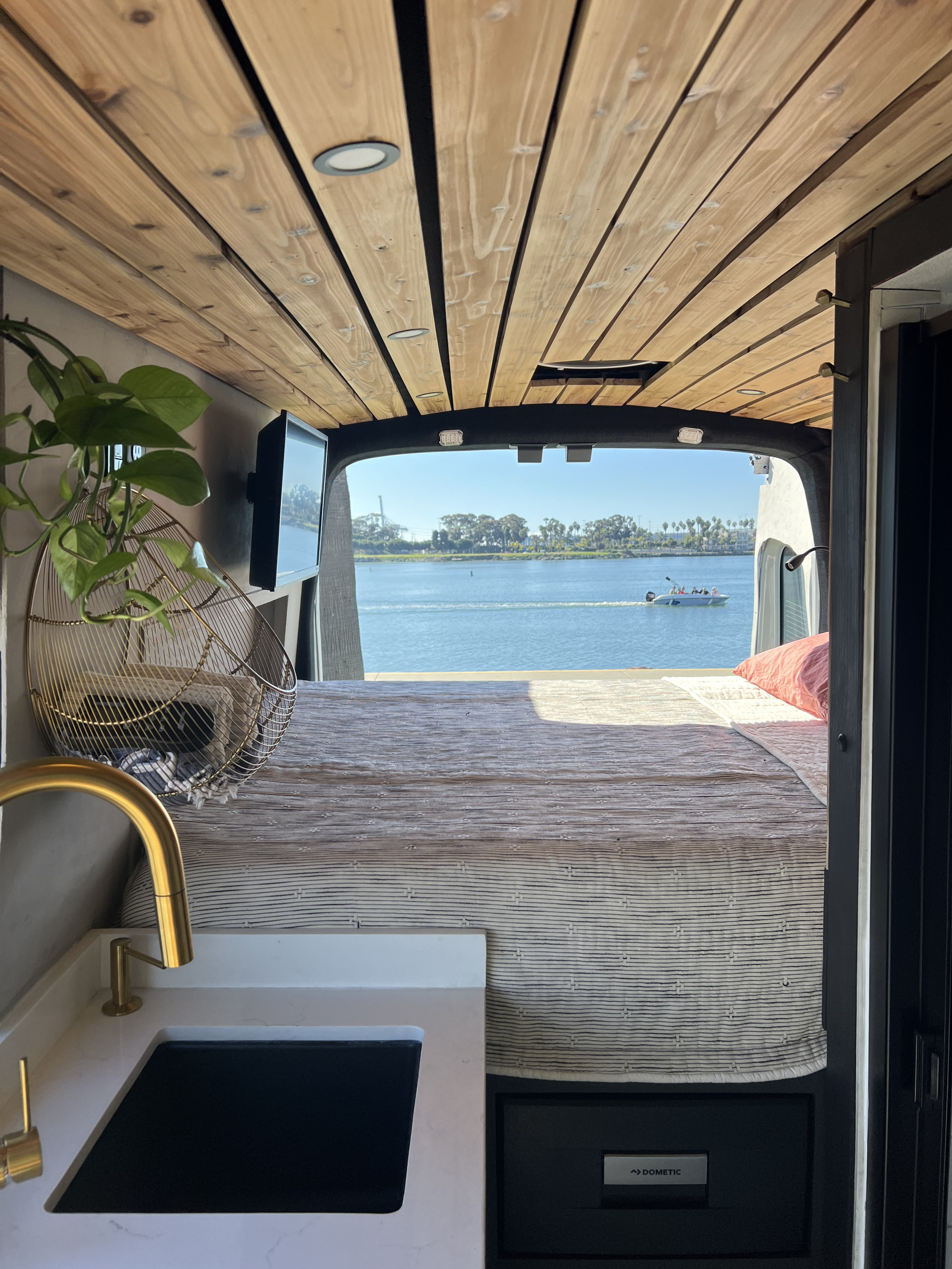 RV rental: Interior shot from the front showing a bed, kitchen counter with gold faucet, and a Dometic fridge, with a stunning water view from the rear.. Ford Transit 2023