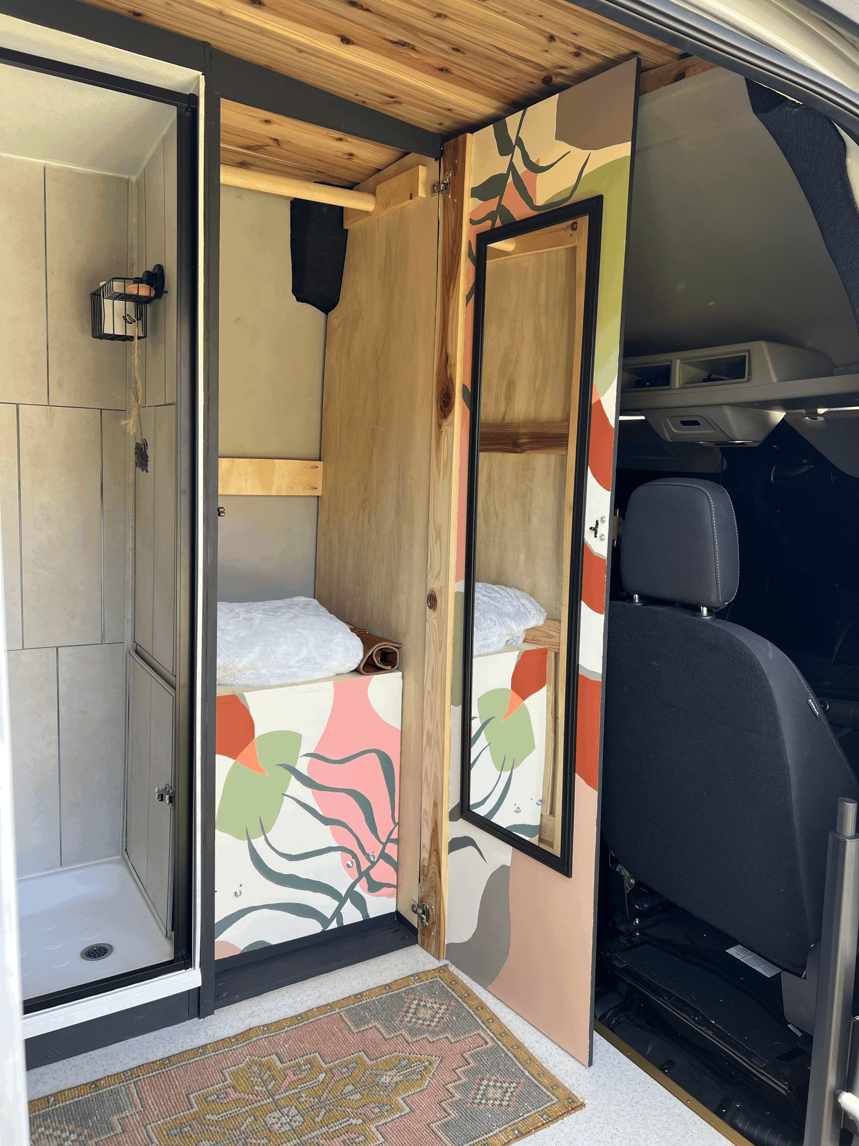 RV rental van conversion with a compact shower, cozy sleeping area, and colorful custom interior design, including a mirrored door.. Ford Transit 2023