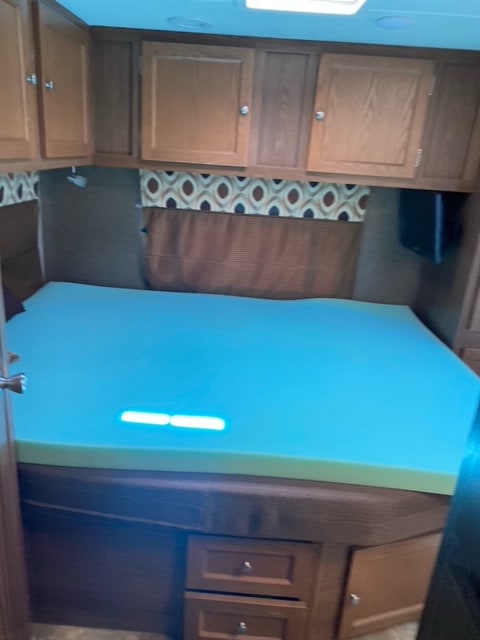 Comfortable RV rental bedroom featuring a spacious blue foam bed, overhead cabinets, and built-in storage.. Coachmen Leprechaun 2017