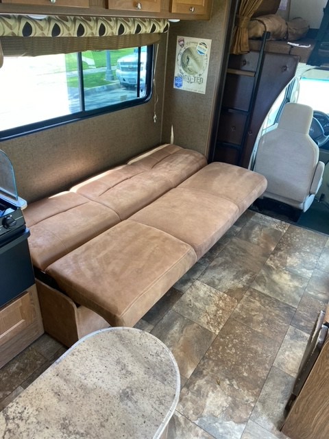 RV rental interior: Extended brown sofa, overhead bunk, and kitchen area for a versatile living space.. Coachmen Leprechaun 2017