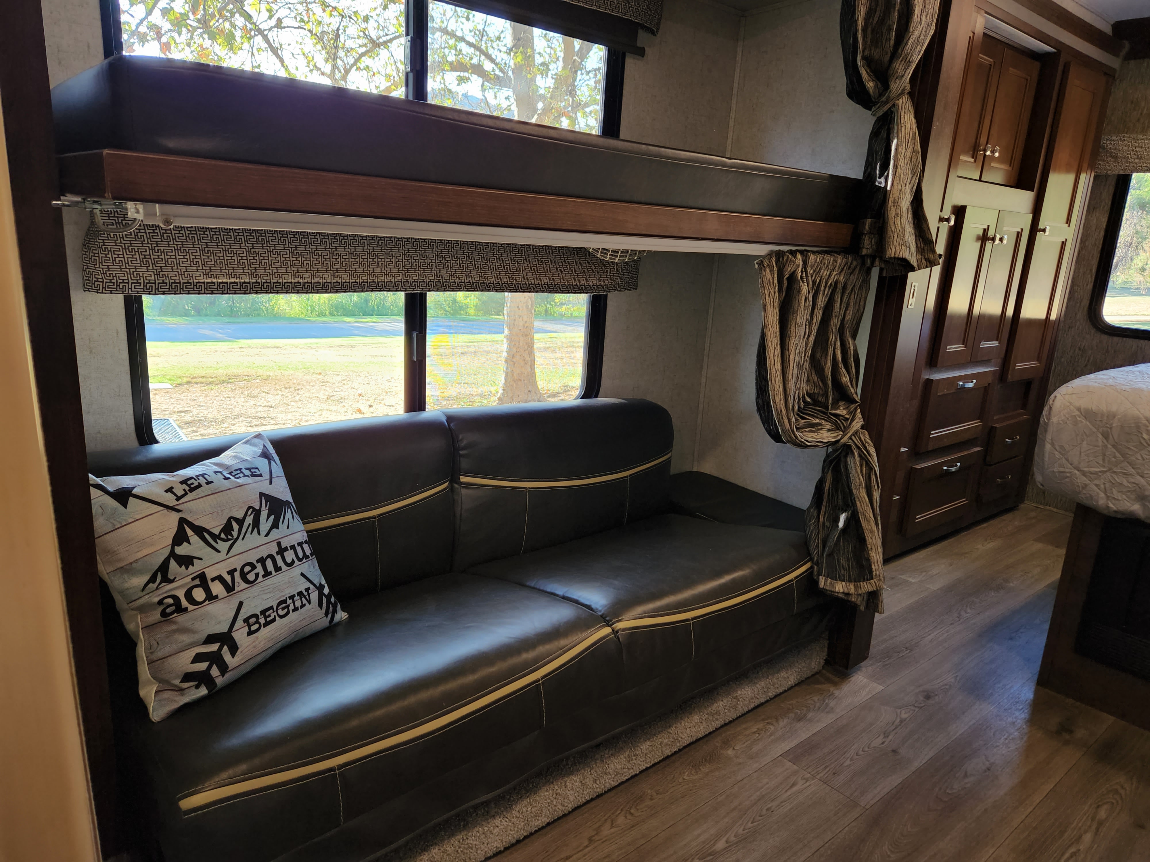 Cozy RV rental interior with a bunk bed, sofa, and cabinets. A pillow reads 'Let the adventure begin'.. Forest River Sunseeker 2018