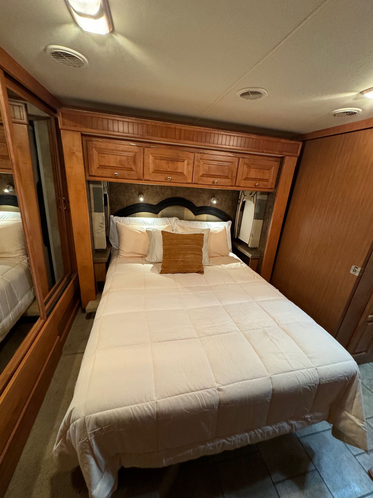Cozy RV rental bedroom featuring a queen bed with light bedding, overhead wooden cabinets, and a mirrored closet.. Allegro Allegro Red 2010