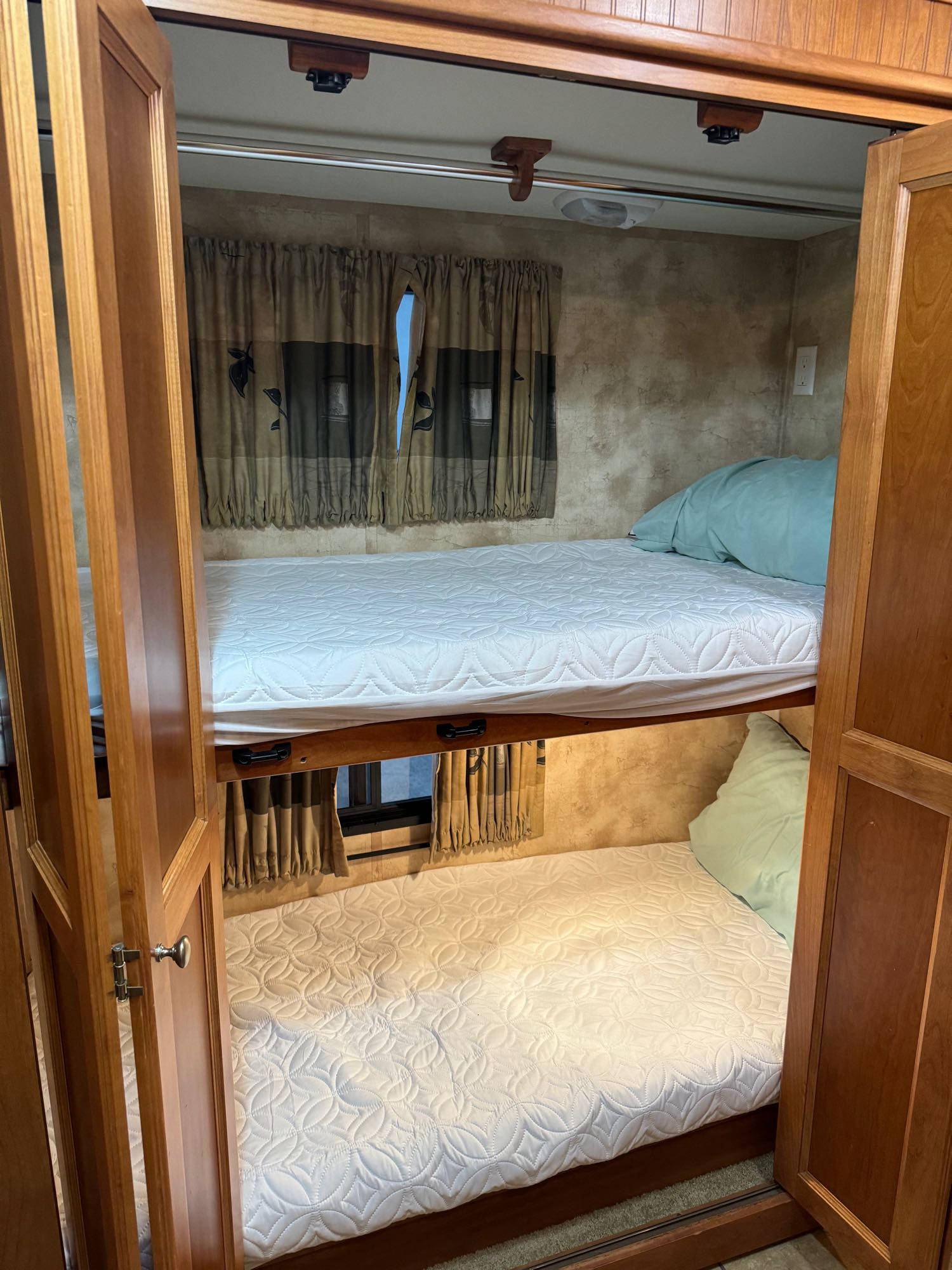 RV rental interior showcasing comfortable bunk beds with white quilted mattresses, light blue pillows, and wooden framing.. Allegro Allegro Red 2010