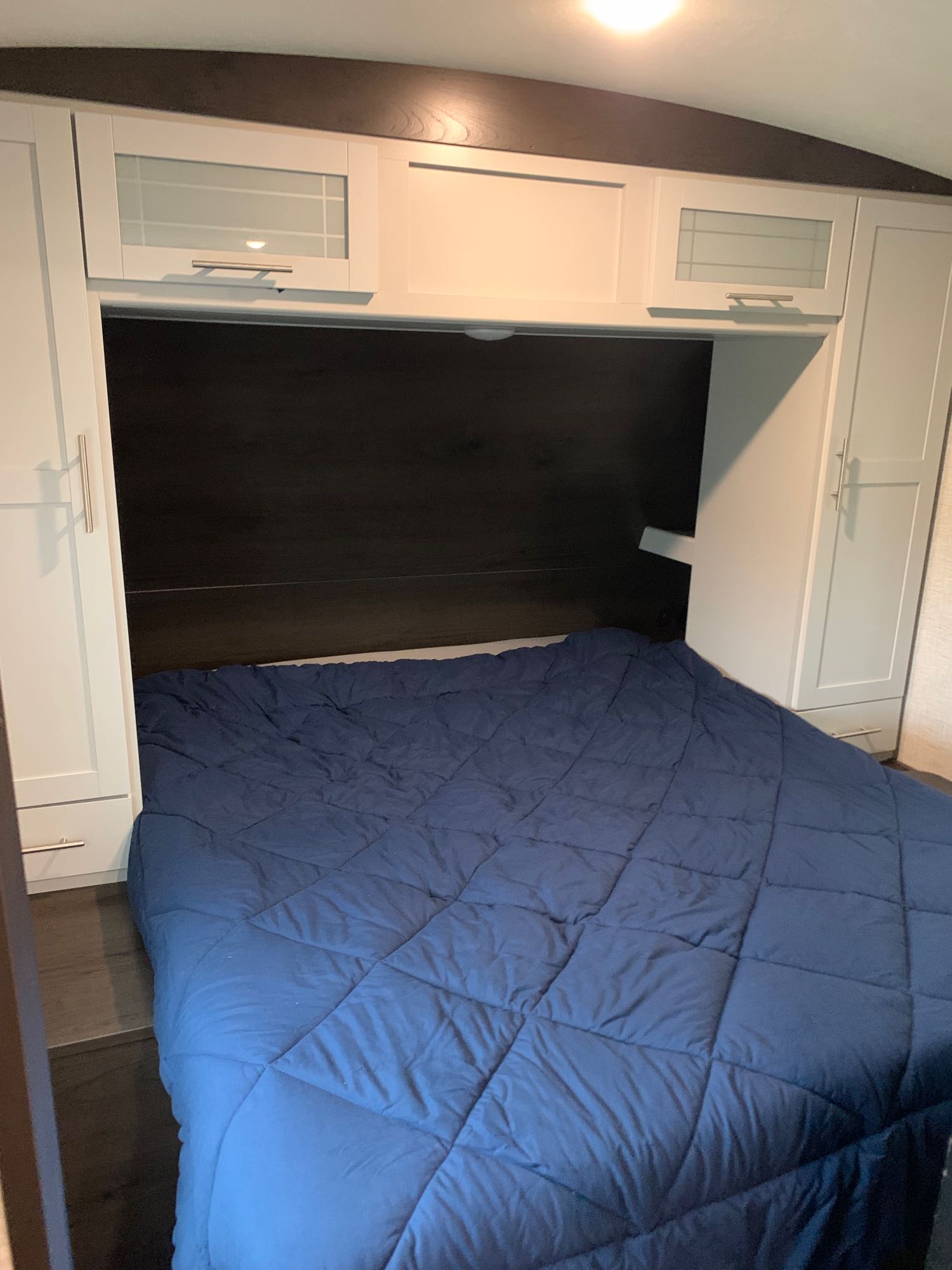 Compact RV rental sleeping area with a blue comforter, white overhead cabinets & wardrobes. Ideal for your next trip.. Keystone RV Bullet Ultra Lite 2021