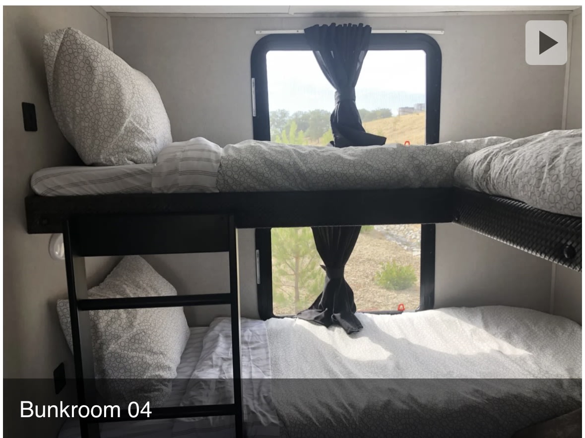 RV rental bunkroom with two cozy bunk beds, patterned bedding, and large windows offering scenic outdoor views.. Forest River Vibe 2020