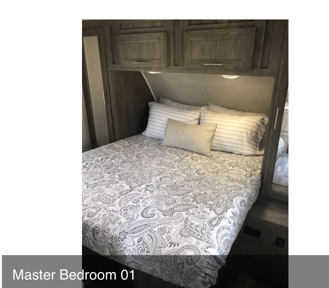 RV rental master bedroom featuring a comfortable bed with paisley bedding, overhead cabinets, and reading lights.. Forest River Vibe 2020