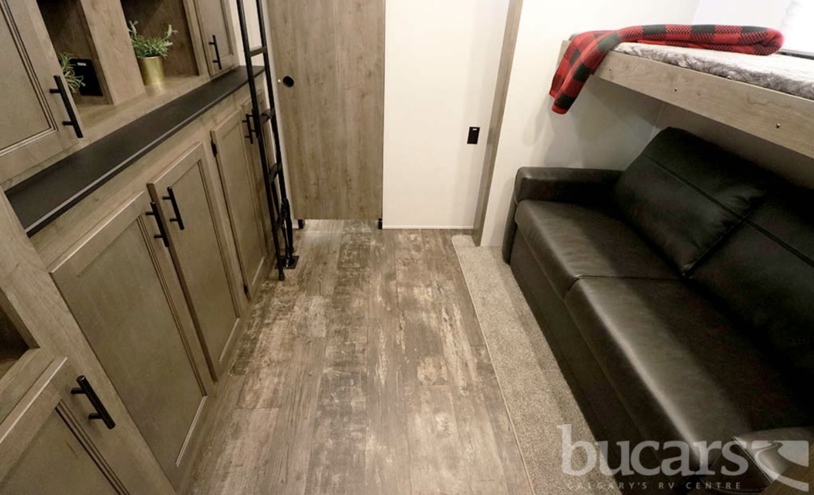 RV rental interior: wood-look flooring, light wood cabinets, leather sofa, and a bunk bed with a cozy red plaid blanket.. Forest River Sabre 2022