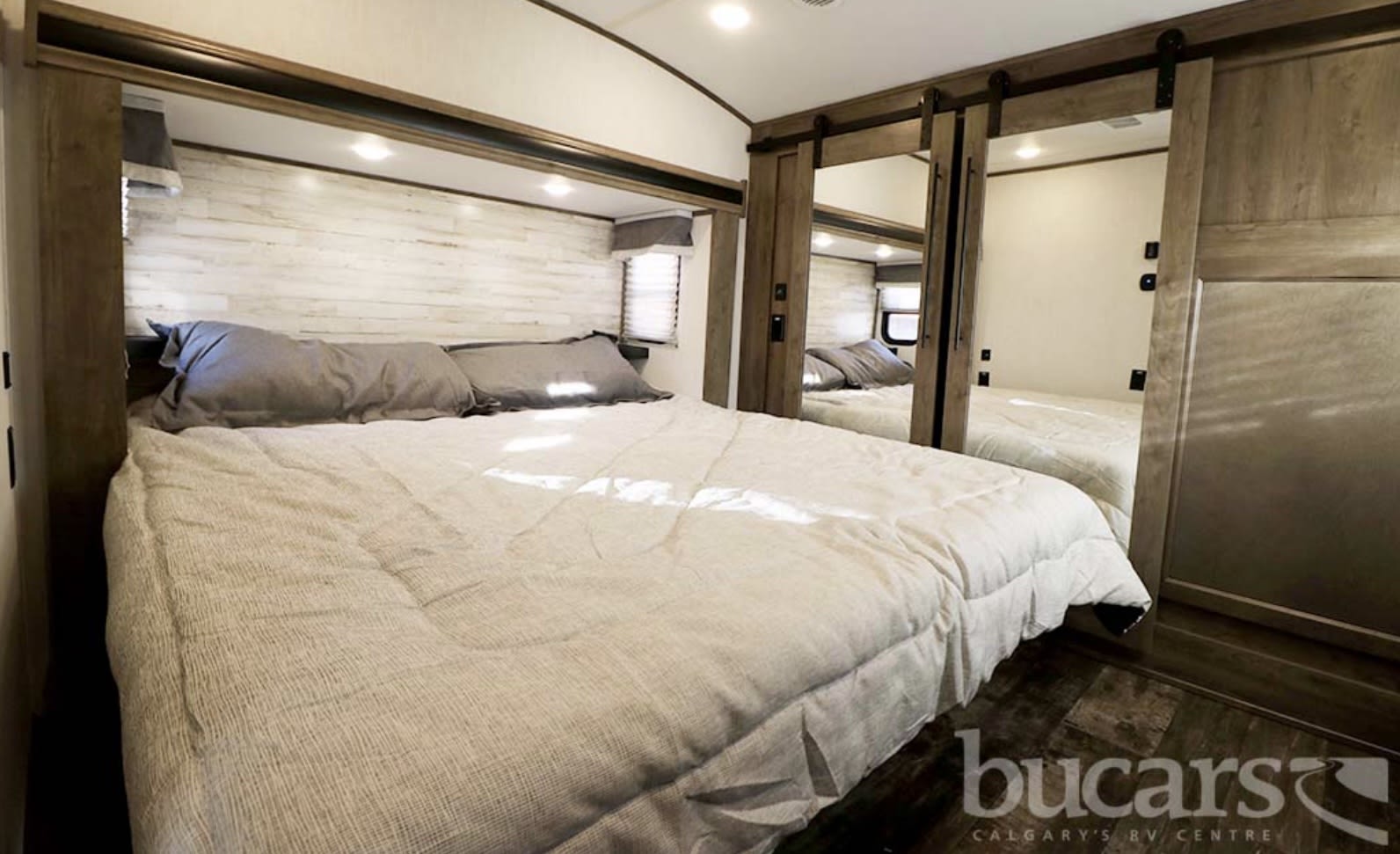 Cozy RV rental bedroom featuring a large bed, white shiplap wall, and mirrored closet doors. Ideal for comfortable travel.. Forest River Sabre 2022