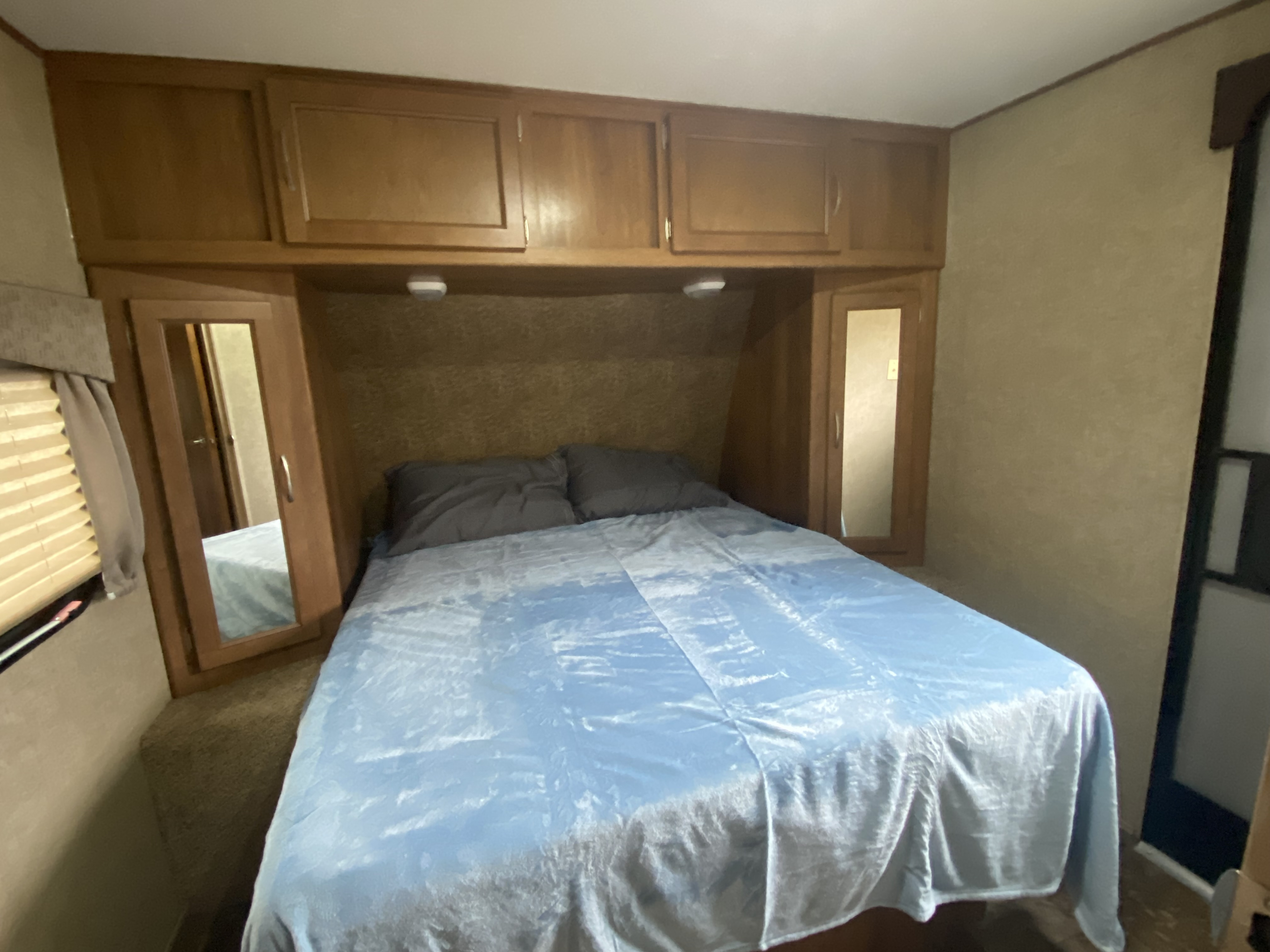 Inside a compact RV rental bedroom featuring a blue bed, overhead wood cabinets, and mirrored storage units.. Coachmen Apex 2014