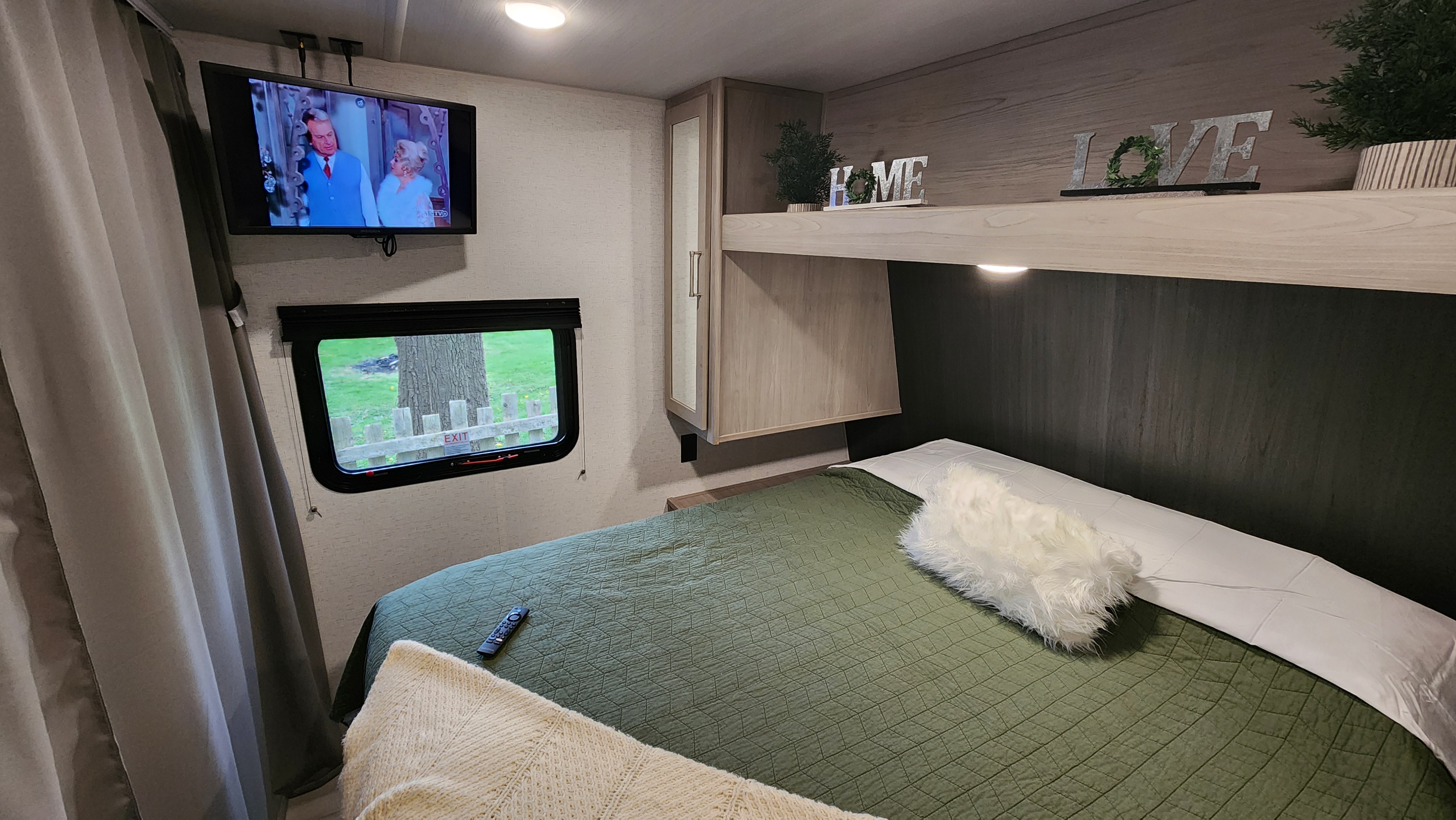 Cozy RV rental bedroom featuring a comfy bed, wall-mounted TV, window view, and practical storage.. Keystone RV Springdale 200RLC 2024