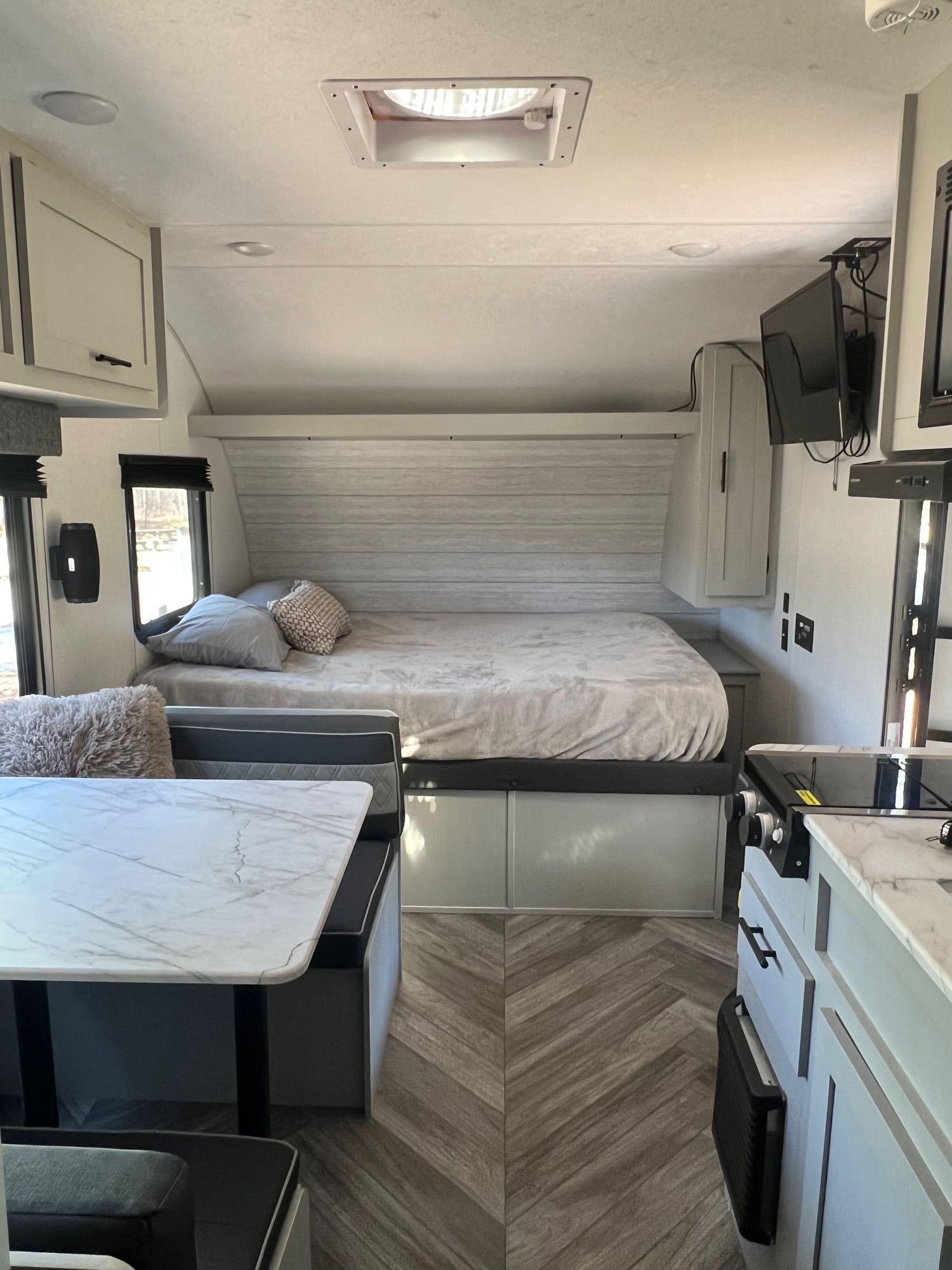 Interior of a modern RV rental, featuring a bed, dinette table, and kitchenette. Light colors and wood floor.. Forest River Salem FSX 2022