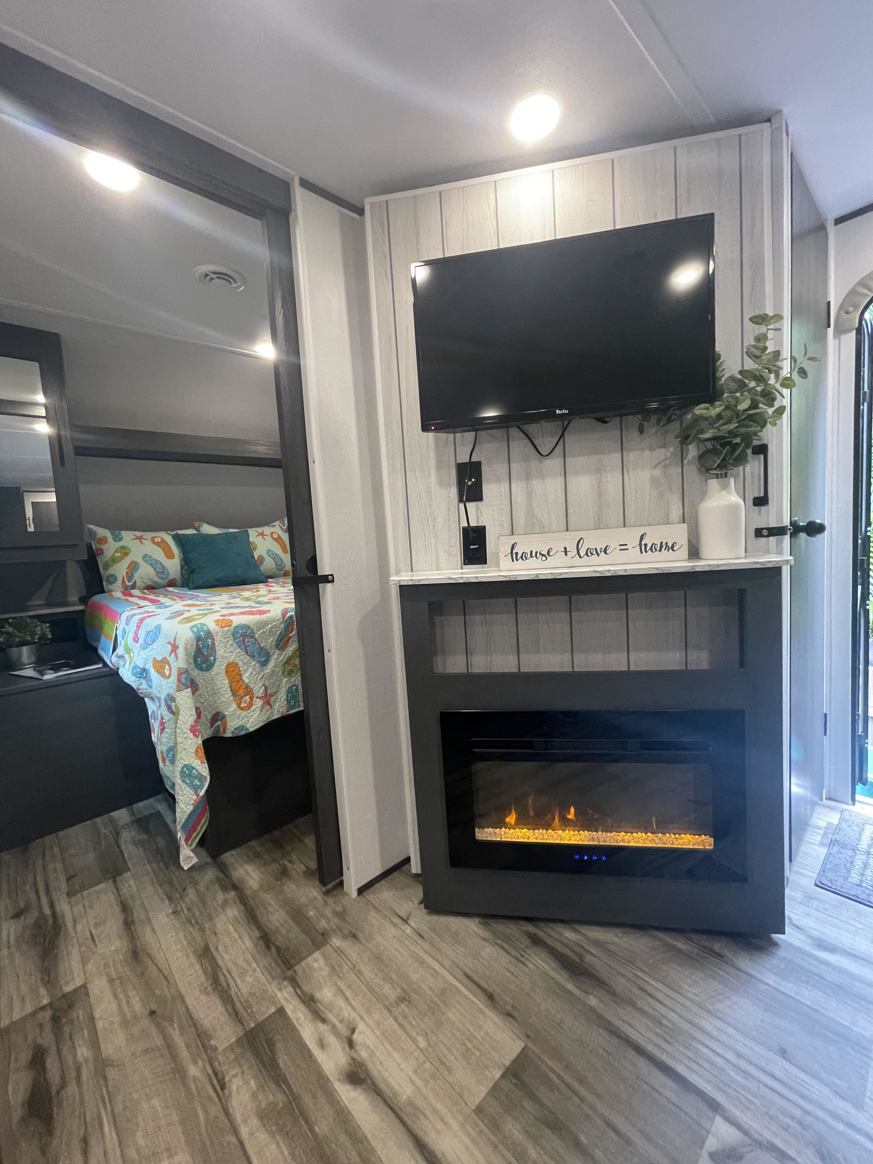 Modern RV rental interior: bedroom with colorful bedding, living area with TV & electric fireplace, wood-look floor.. Dutchmen Aspen Trail 2024