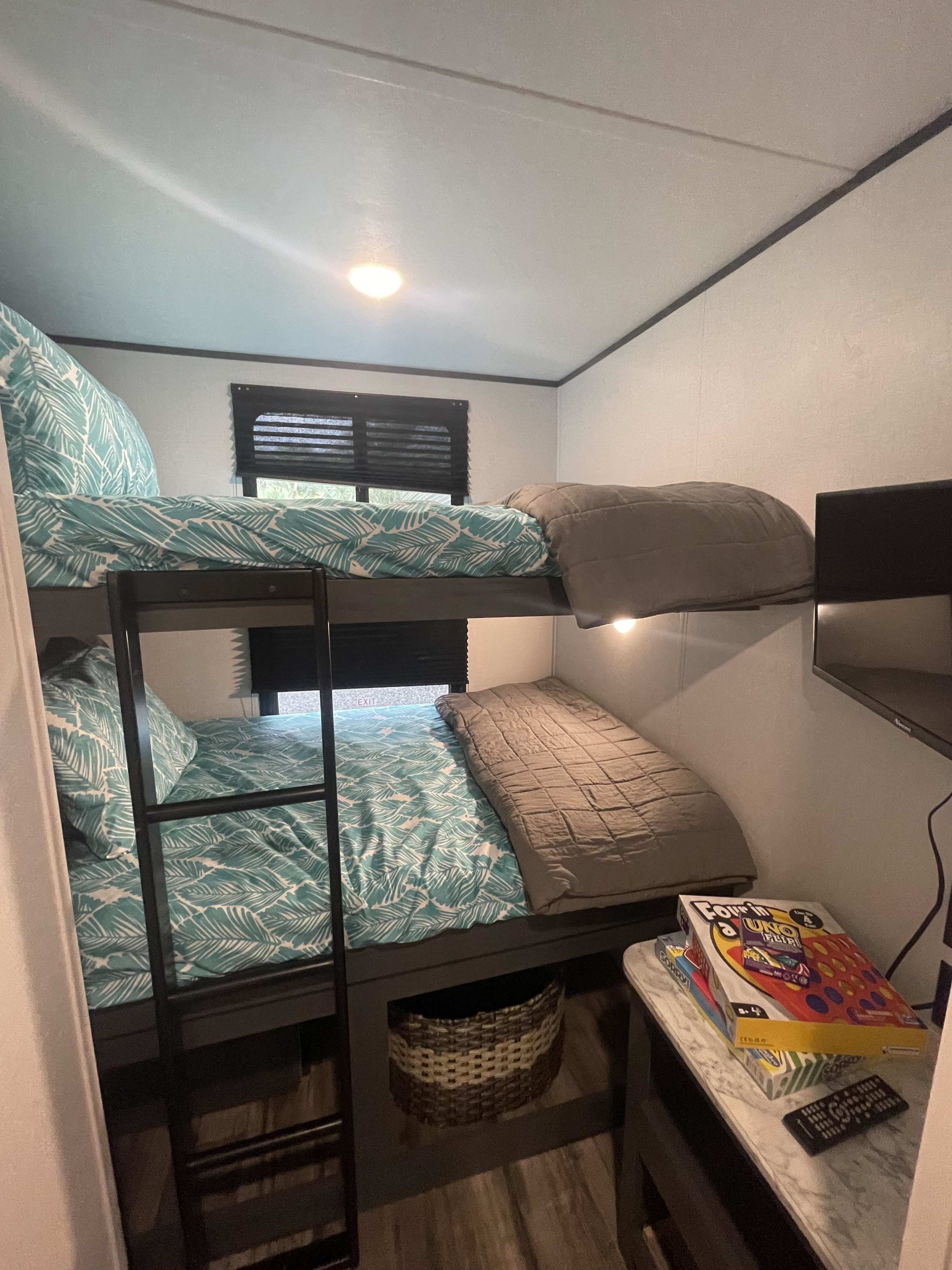 Cozy RV rental bunk beds feature teal leaf bedding, a TV, and board games for guest enjoyment.. Dutchmen Aspen Trail 2024