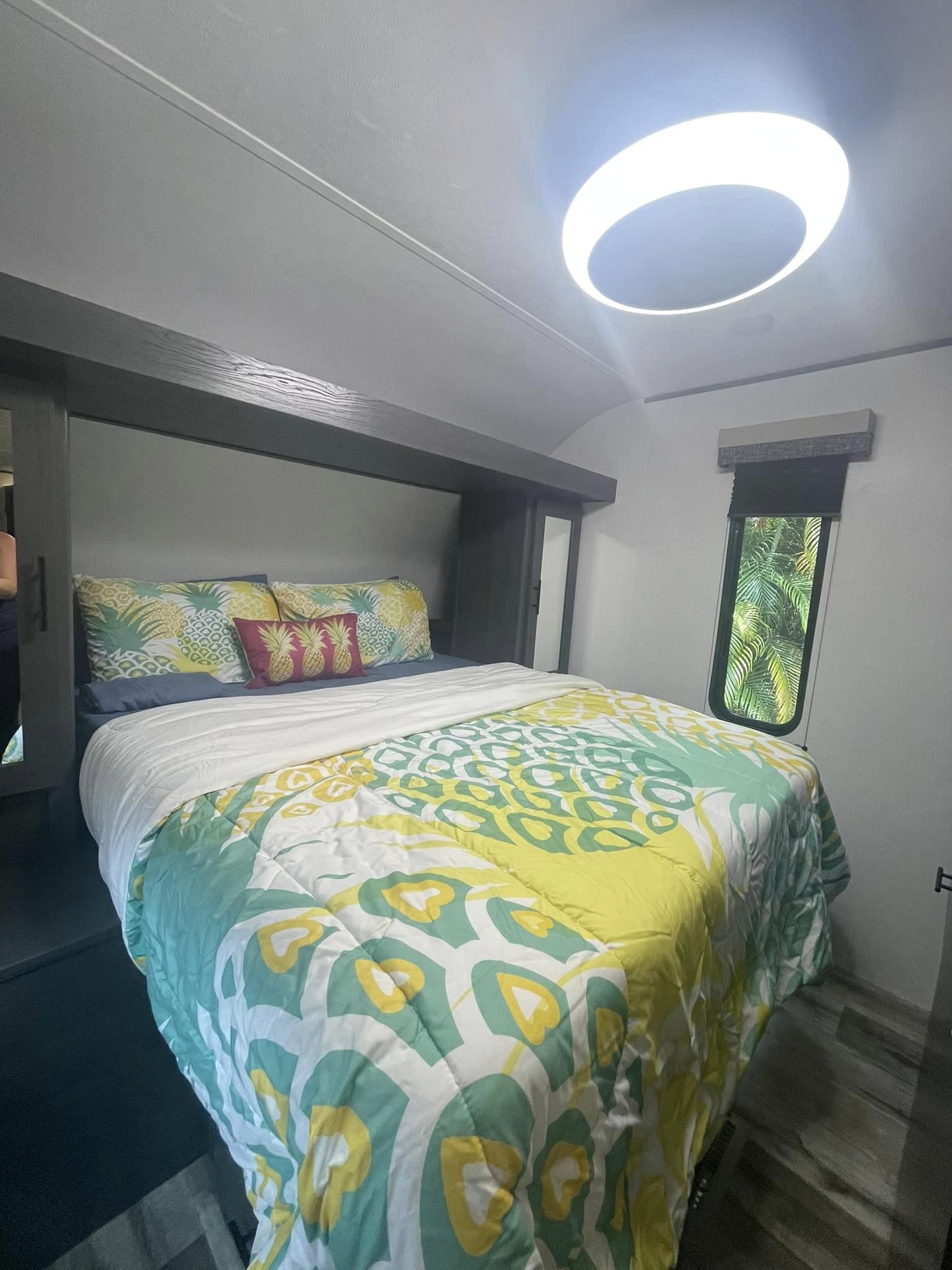 Cozy RV rental bedroom featuring vibrant pineapple bedding and a window with lush tropical views, ideal for travel comfort.. Dutchmen Aspen Trail 2024
