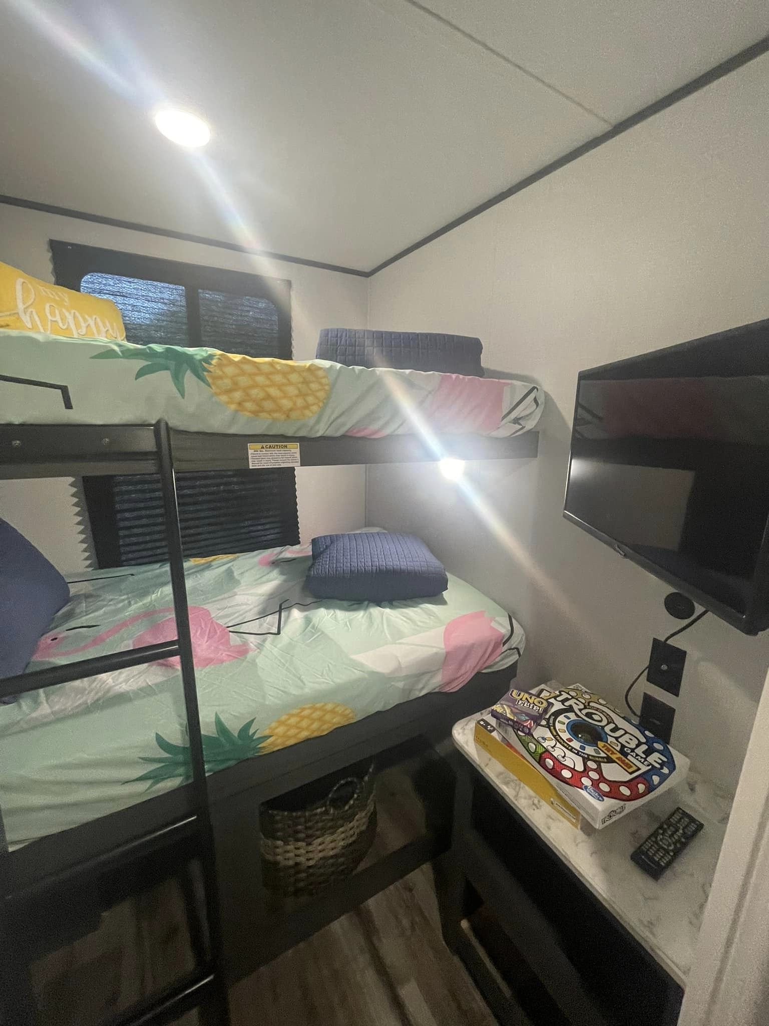 RV rental bunk beds with patterned bedding, a wall-mounted TV, and board games on a nightstand.. Dutchmen Aspen Trail 2024