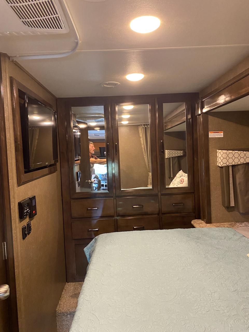RV rental bedroom: cozy space with a light blue bed, mounted TV, and wood-toned mirrored dresser/closet.. Thor Quantum 2020
