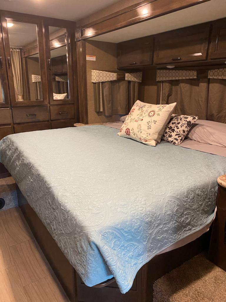 Cozy RV rental bedroom featuring a light blue patterned bedspread, throw pillows, and mirrored storage.. Thor Quantum 2020