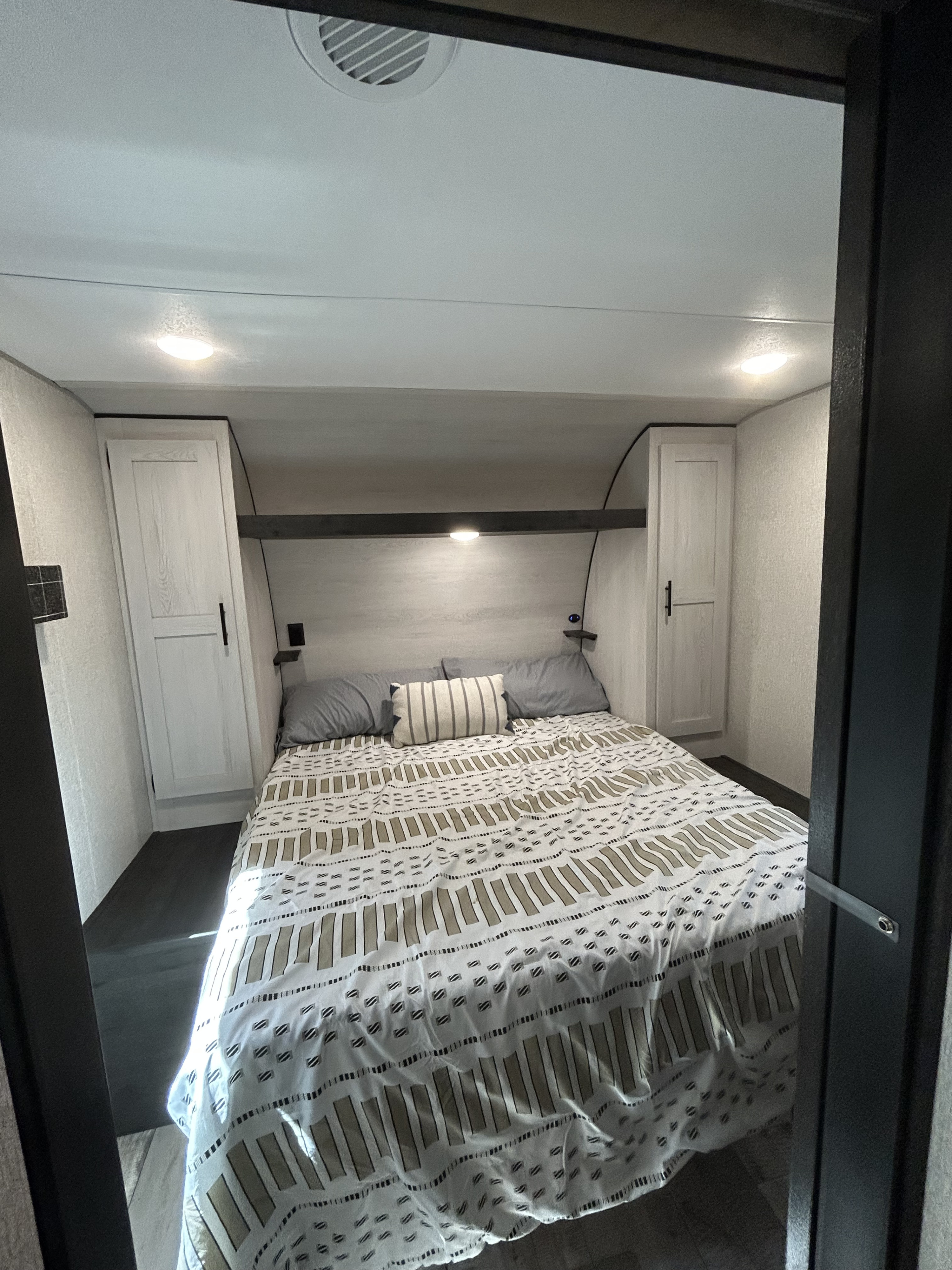 Cozy RV rental bedroom with a queen bed, modern white cabinets, and bright overhead lighting, perfect for travel comfort.. KZ Sportsmen SE 2022