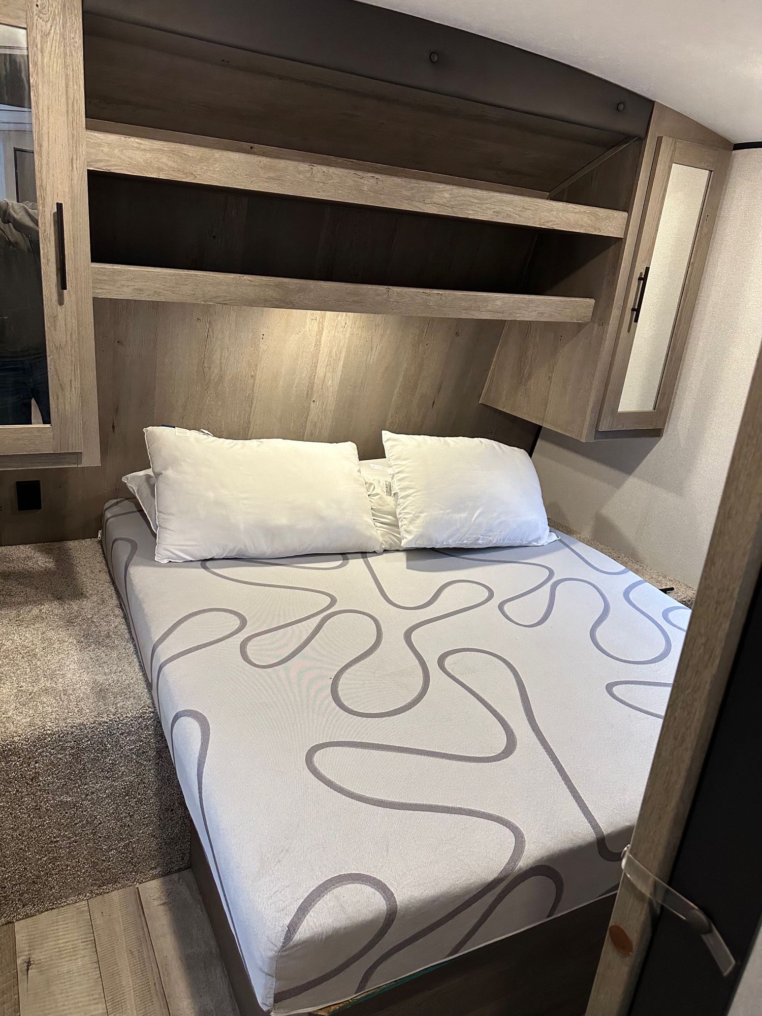 An RV rental bedroom: a comfortable bed with a patterned mattress, overhead shelves, and mirrored cabinets for ample storage.. Keystone RV Springdale 2021