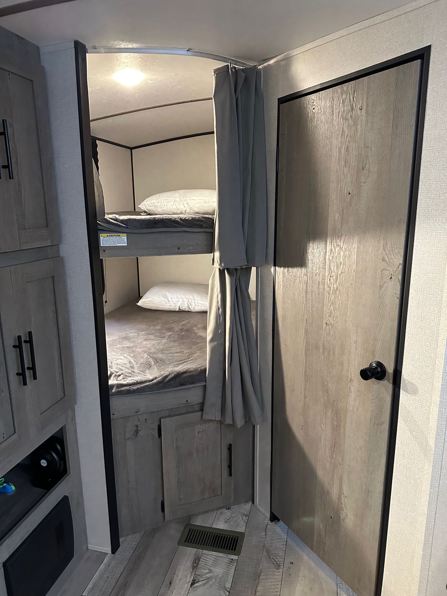 Inside an RV rental: Compact bunk beds with gray curtains, a door, and cabinets. Ideal sleeping area for family road trips.. Keystone RV Springdale 2021