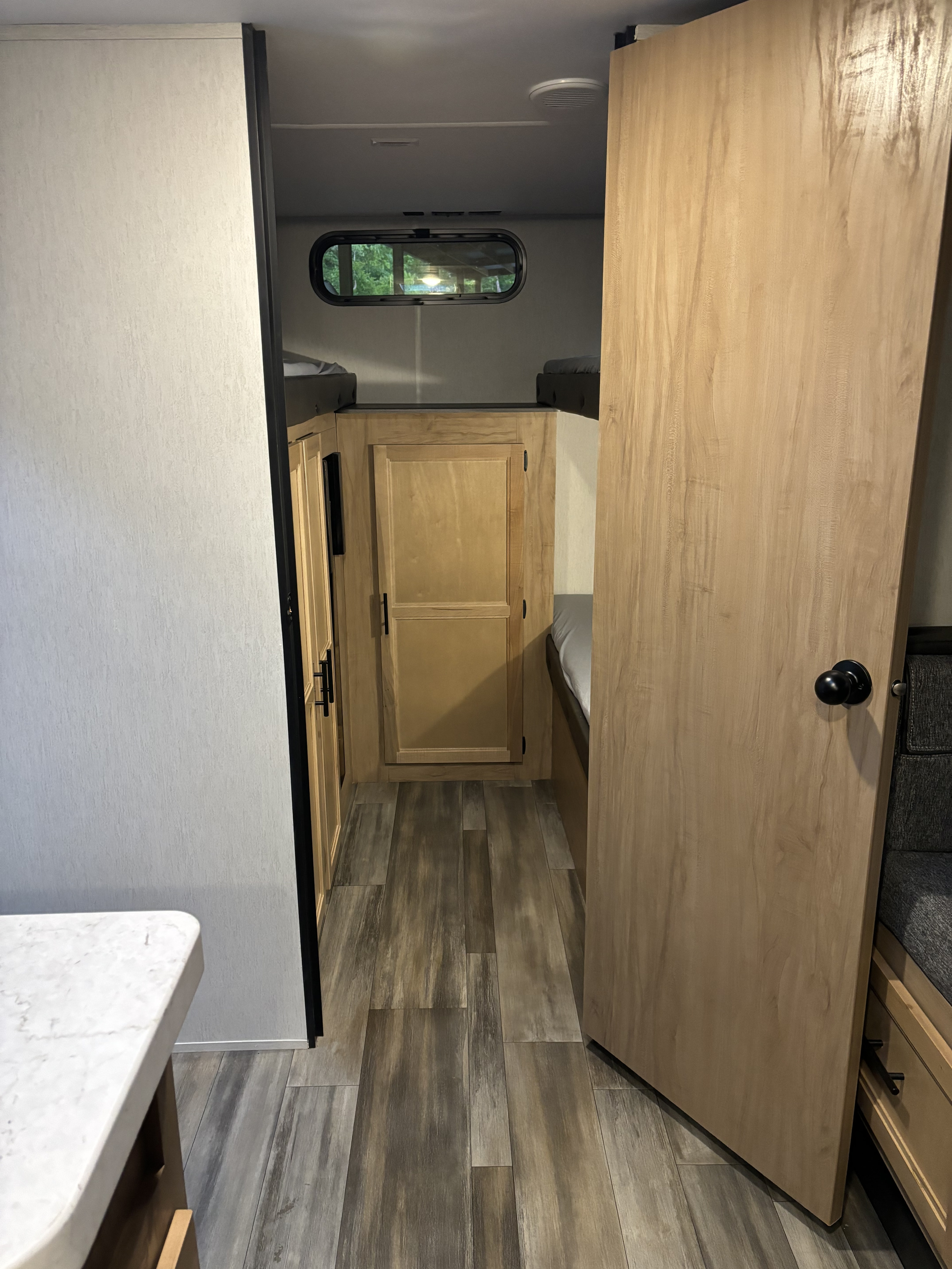 RV rental interior: A hallway leads to cozy bunk beds and built-in storage, featuring modern wood-look flooring.. Forest River Cherokee Grey Wolf 2023