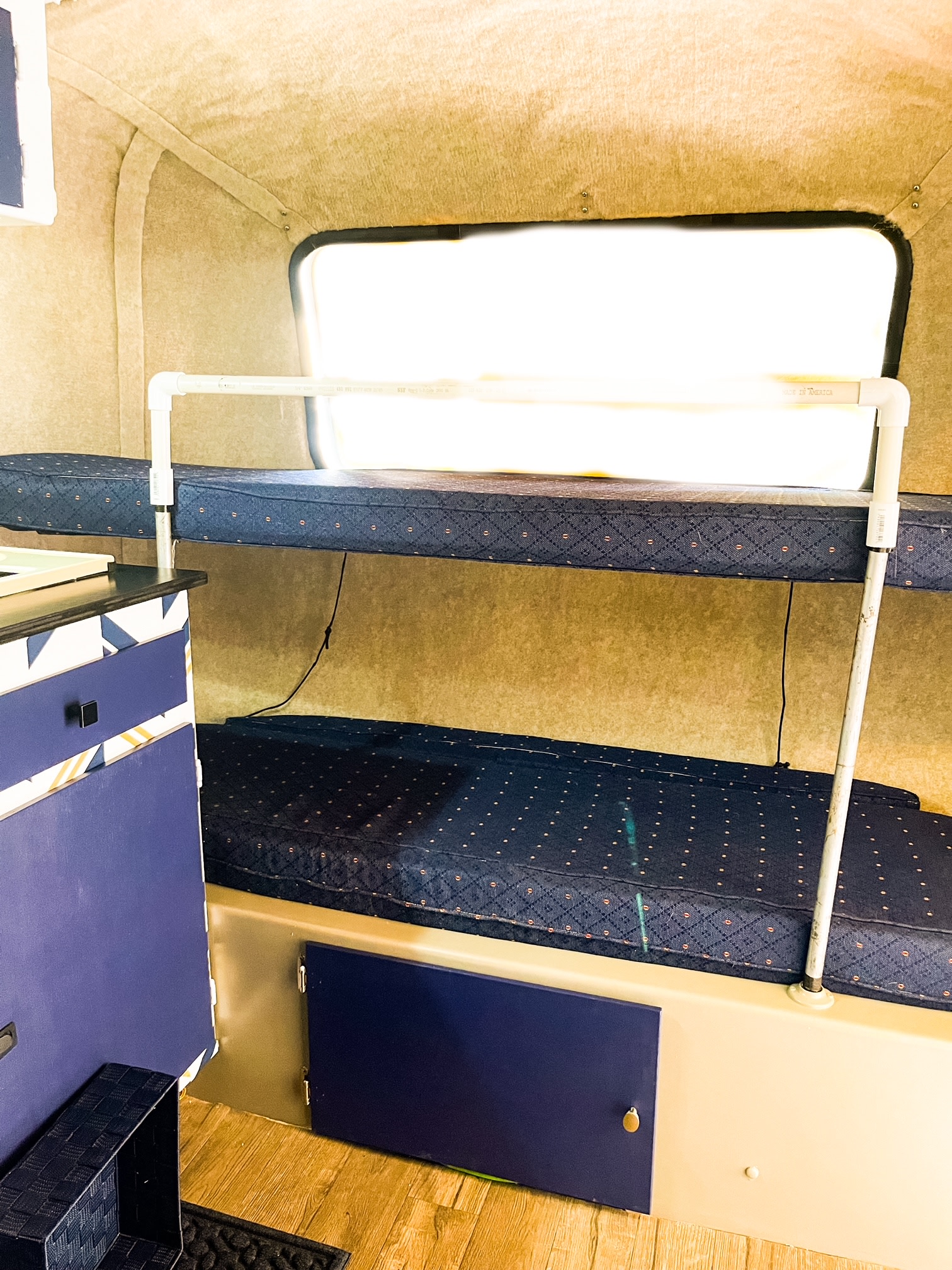 Compact RV rental interior featuring two bunk beds with blue mattresses, white PVC safety rail, and lower storage.. Scamp 13' 1988