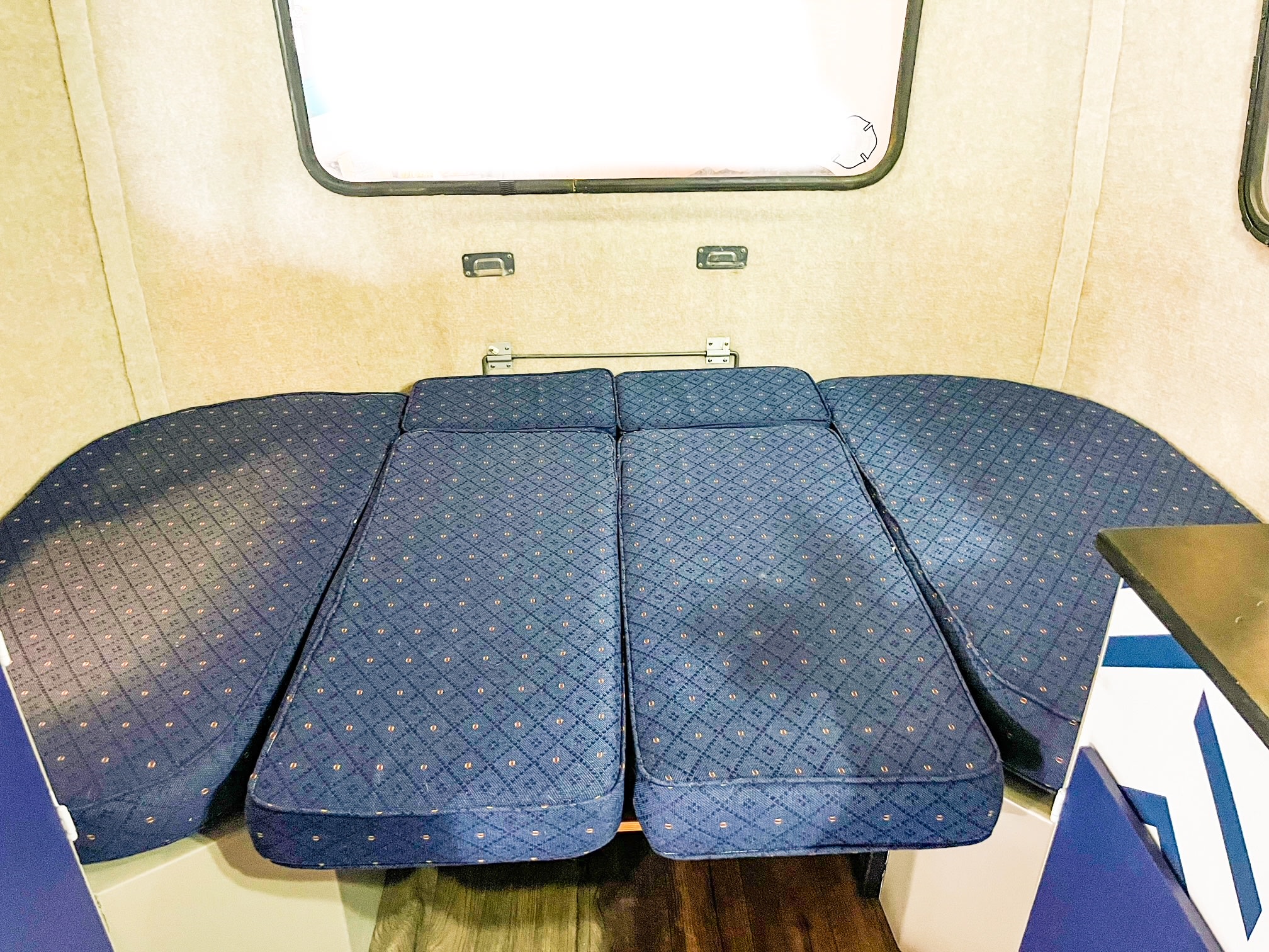 RV rental interior showing a convertible dinette bed with blue patterned cushions in a cozy camper.. Scamp 13' 1988