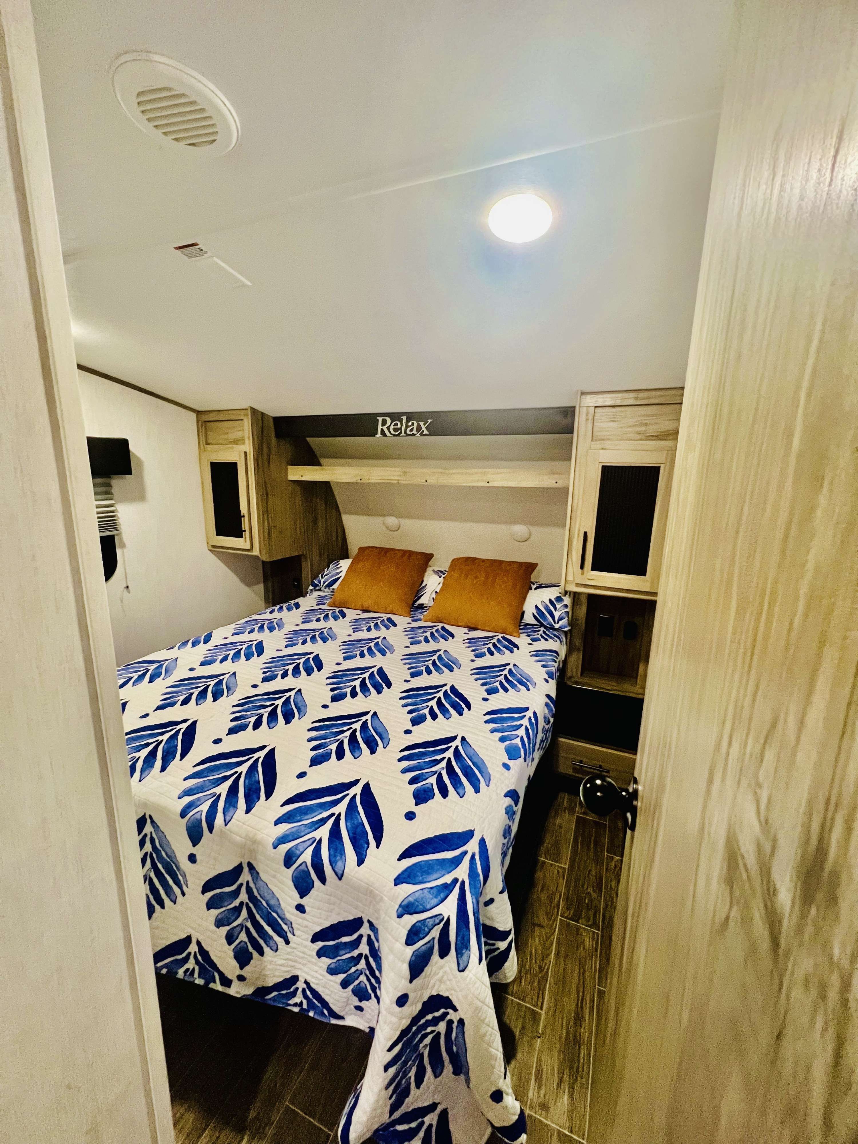 Cozy RV rental bedroom: blue leaf quilt, orange pillows, and "Relax" sign above the bed.. Forest River Cherokee Arctic Wolf 2021