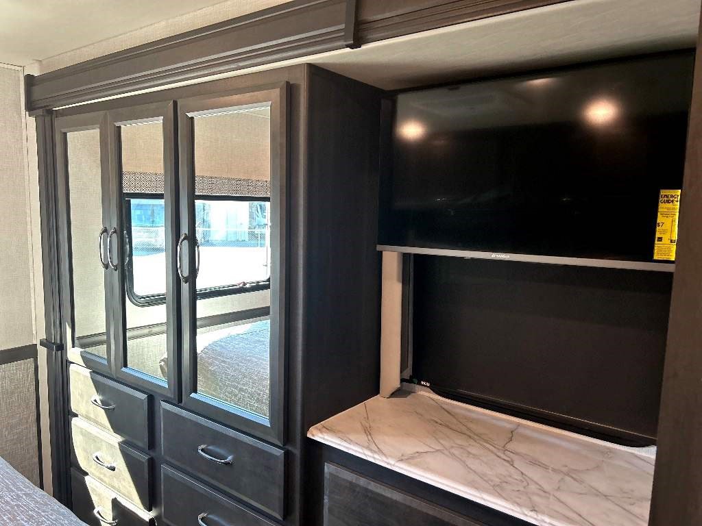 Inside your RV rental: a compact bedroom with built-in mirrored wardrobe, drawers, and an entertainment system with a flat-screen TV.. Fleetwood Flex 2024