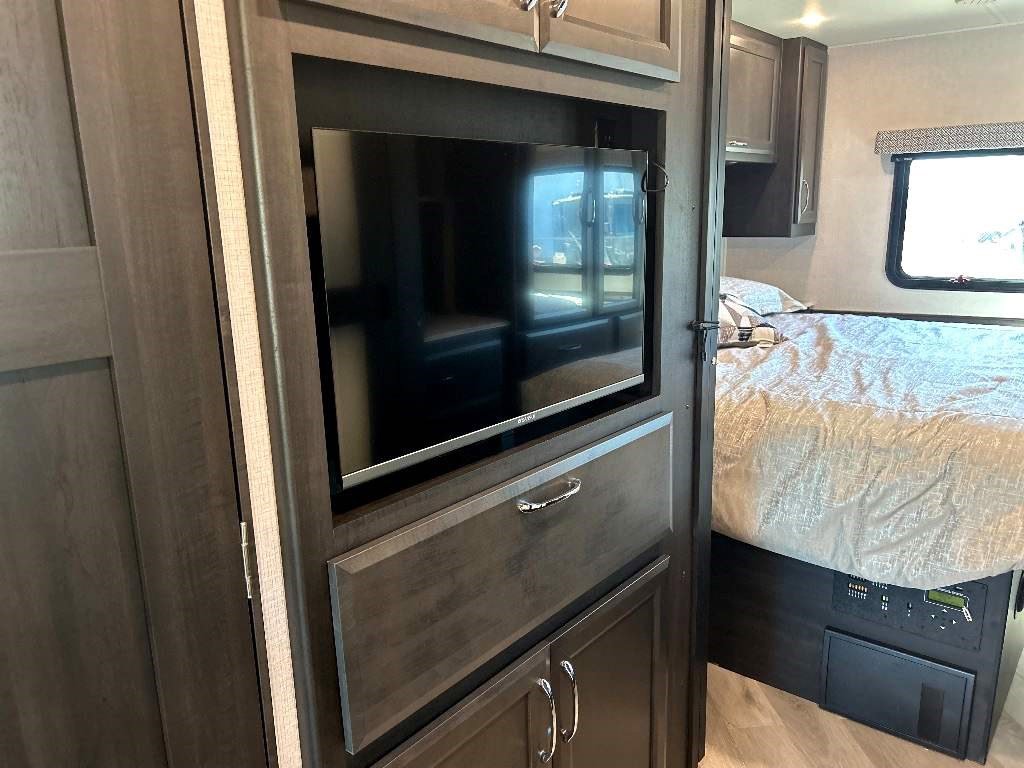 An RV rental's cozy bedroom showcasing a built-in TV, storage, and accessible control panel.. Fleetwood Flex 2024