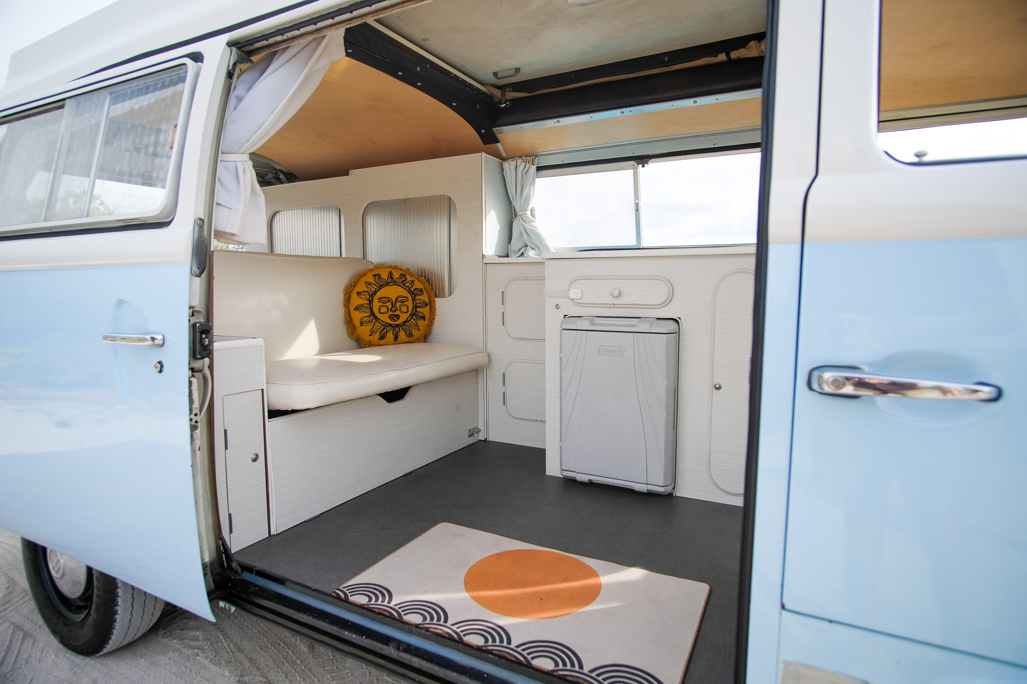 Explore the inviting interior of this light blue RV rental: bench seating, Coleman cooler, and sunny details.. Volkswagen T2 Westfalia 1976
