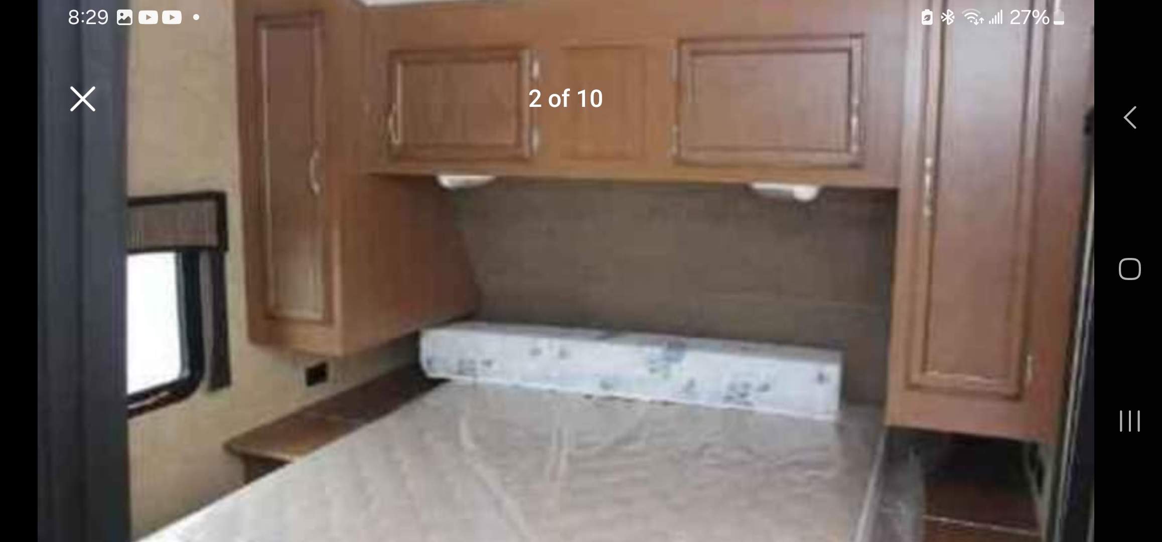 View inside an RV rental bedroom showing a bed with a protective mattress cover, wood overhead cabinets, and a side window.. StarCraft autumn ridge 2014