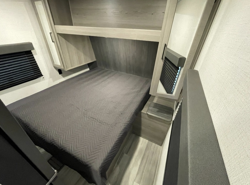 RV rental bedroom featuring a gray bed, overhead storage, window blinds, and mirrored cabinet.. Keystone RV HIDEOUT 31BRD 2024