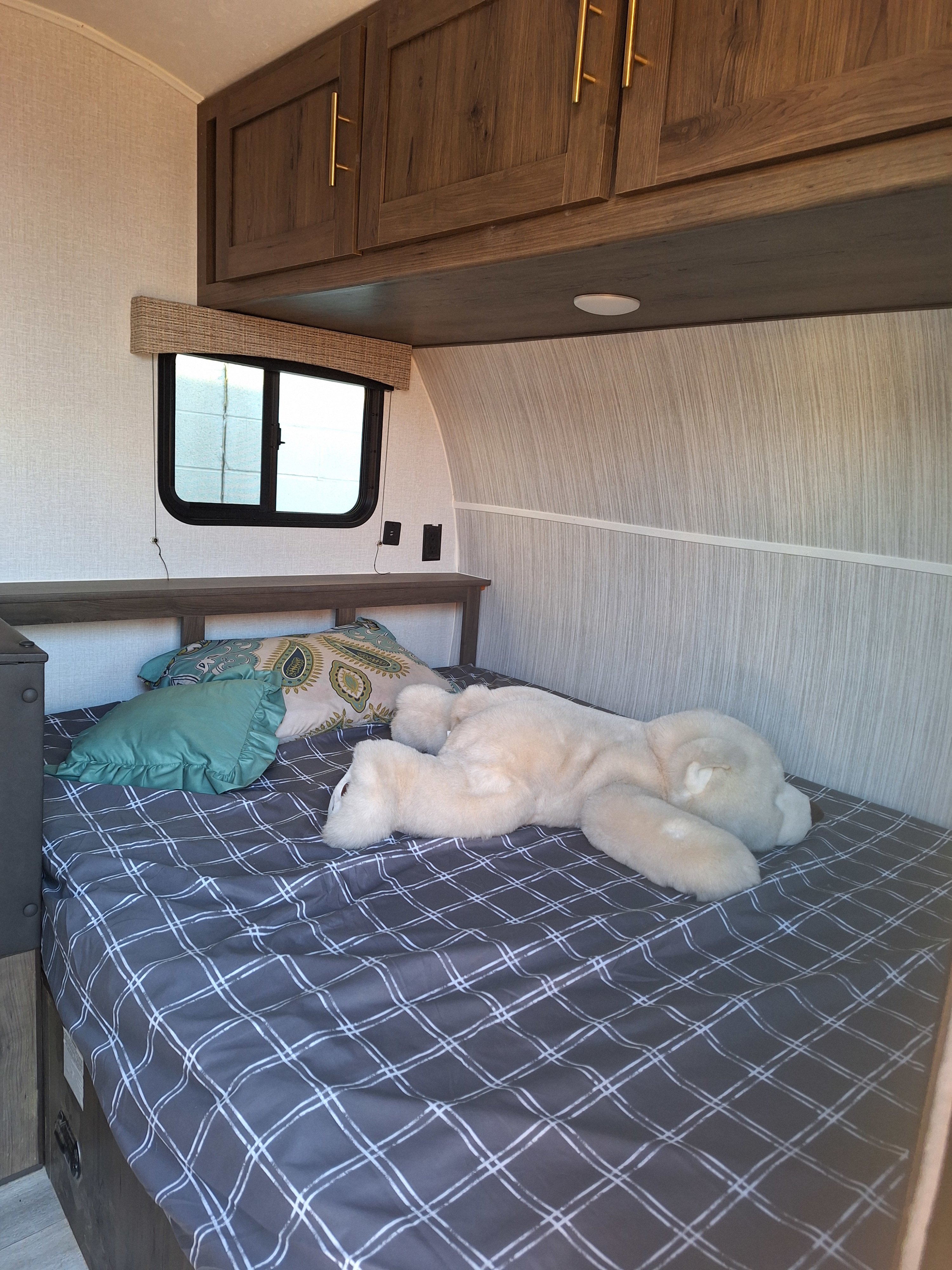 Cozy RV rental bedroom with a comfy bed, plaid comforter, pillows, and a large plush toy. Overhead cabinets & window.. Forest River Viking 2022